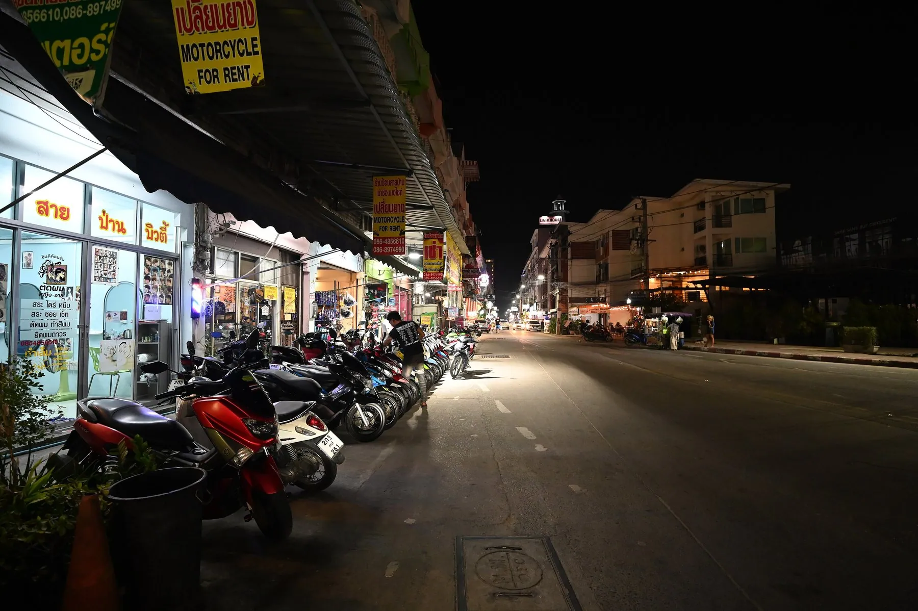 A rank of scooters parked outside lit shopfronts at night beneath a yellow motorcycle for rent sign