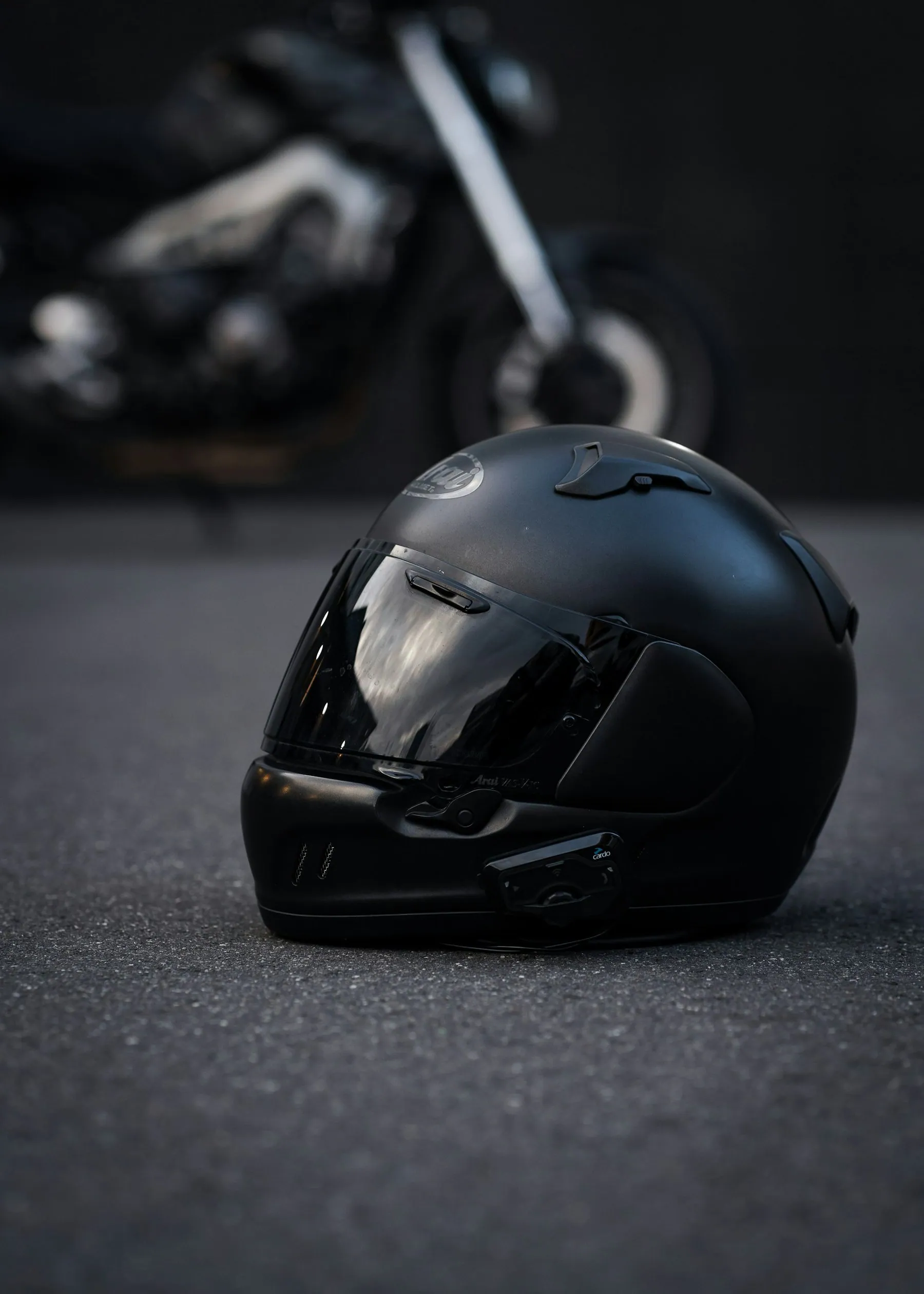 A black full-face helmet resting on the tarmac beside the wheel of a motorbike
