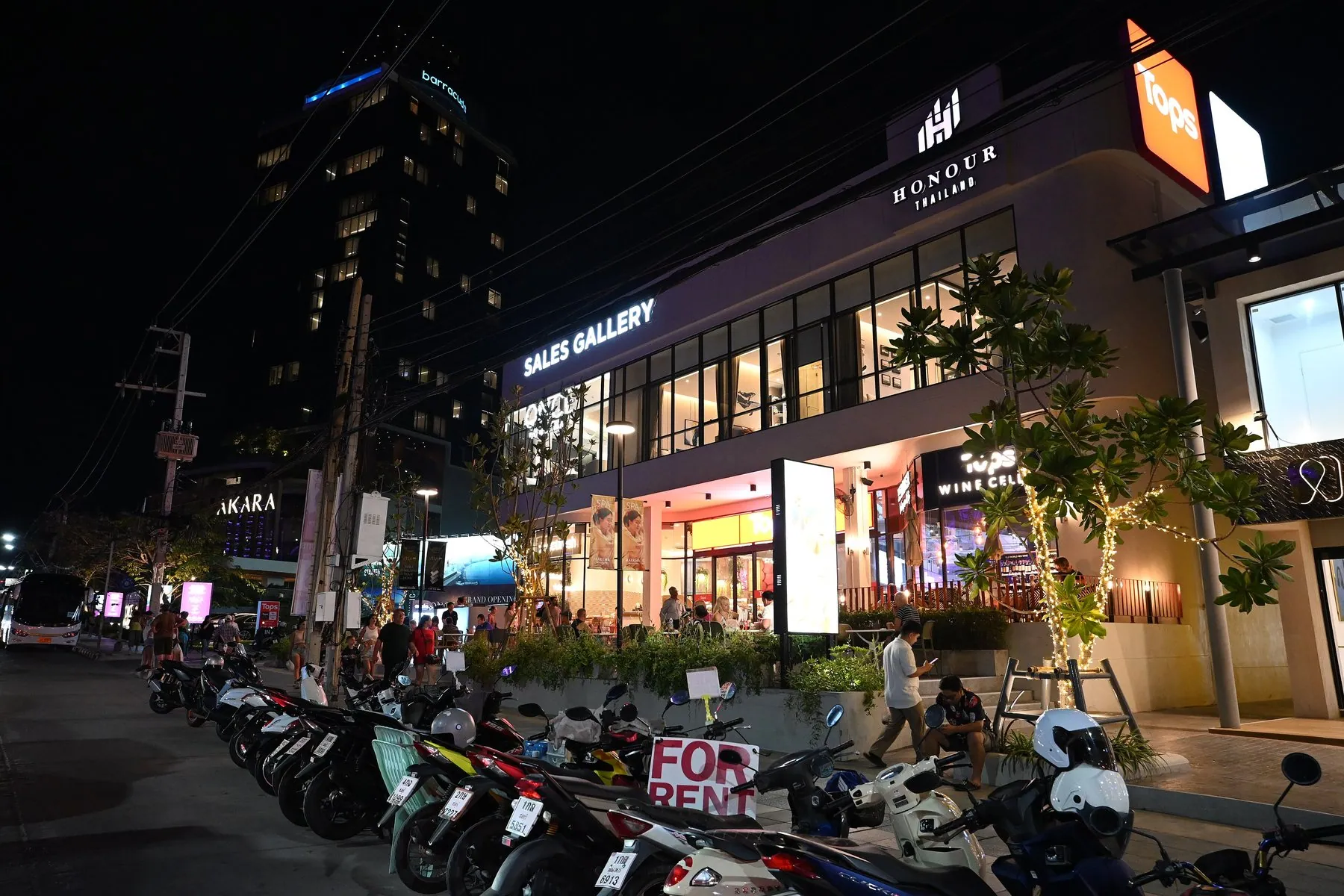 Scooters with for rent boards propped against them, parked outside lit shopfronts on Pattaya's main strip