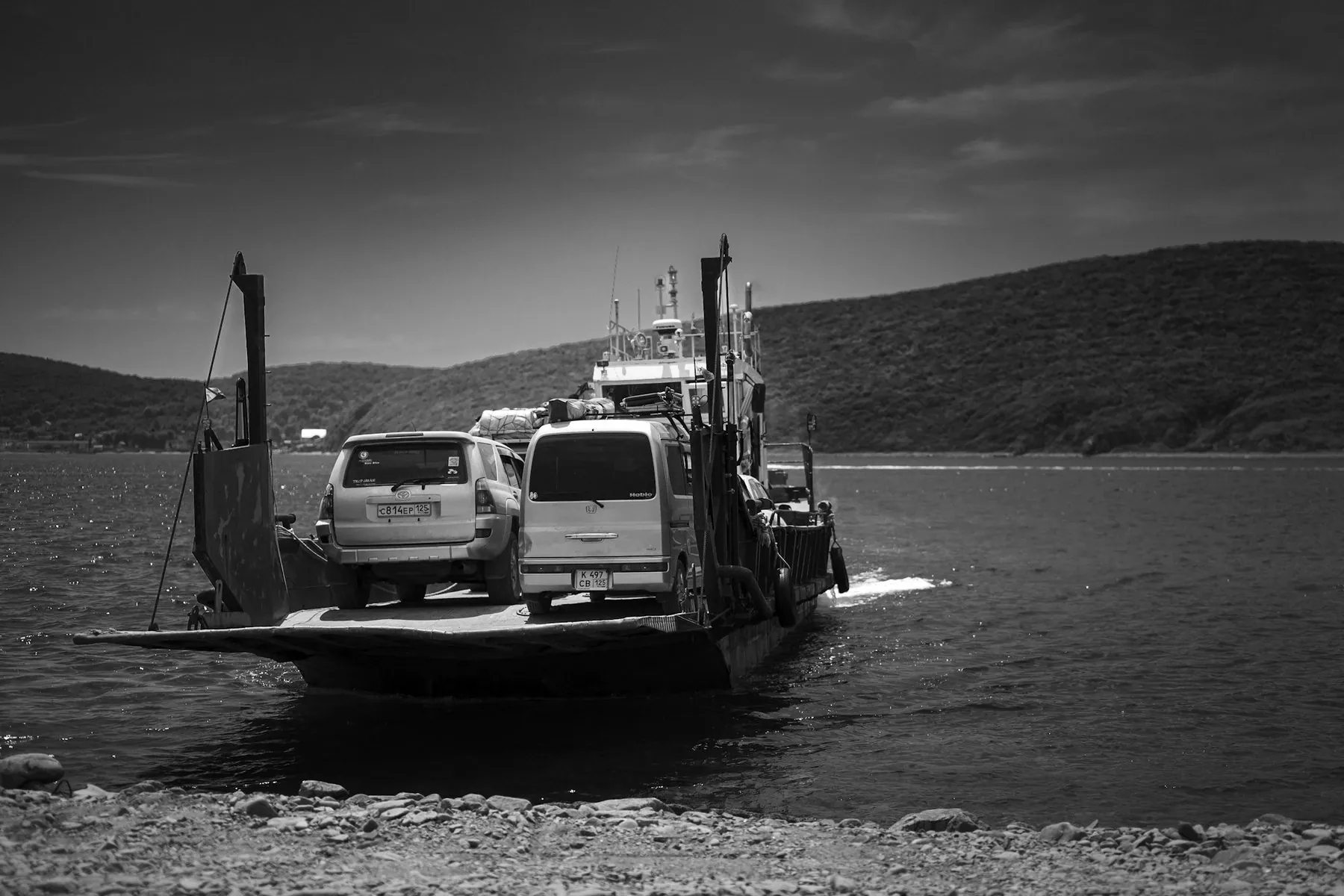 A flat-decked vehicle ferry crossing open water with cars and vans loaded on the bow