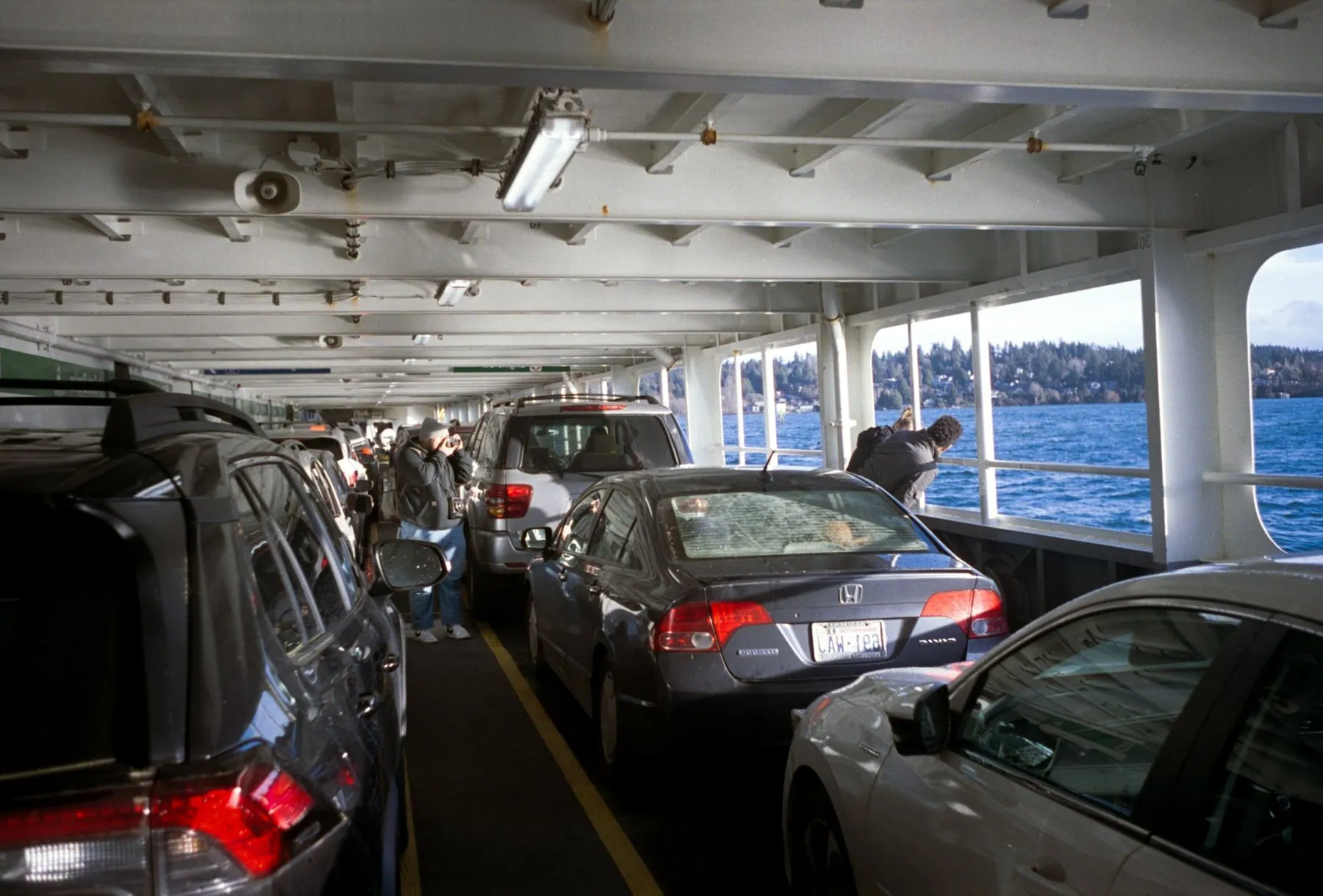 Cars packed nose to tail on a ferry car deck with the sea visible through the side opening