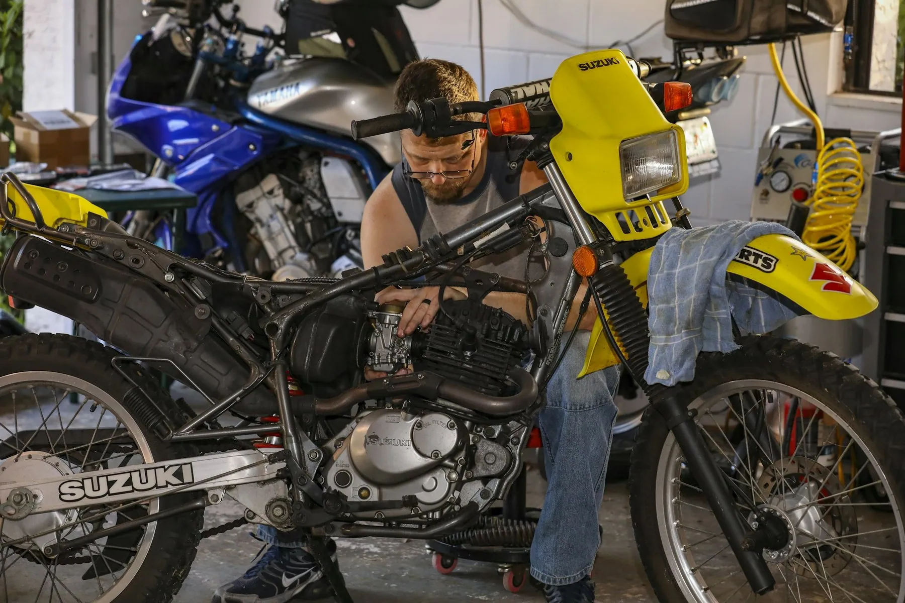 A mechanic bent over the engine of a dismantled motorbike in a workshop