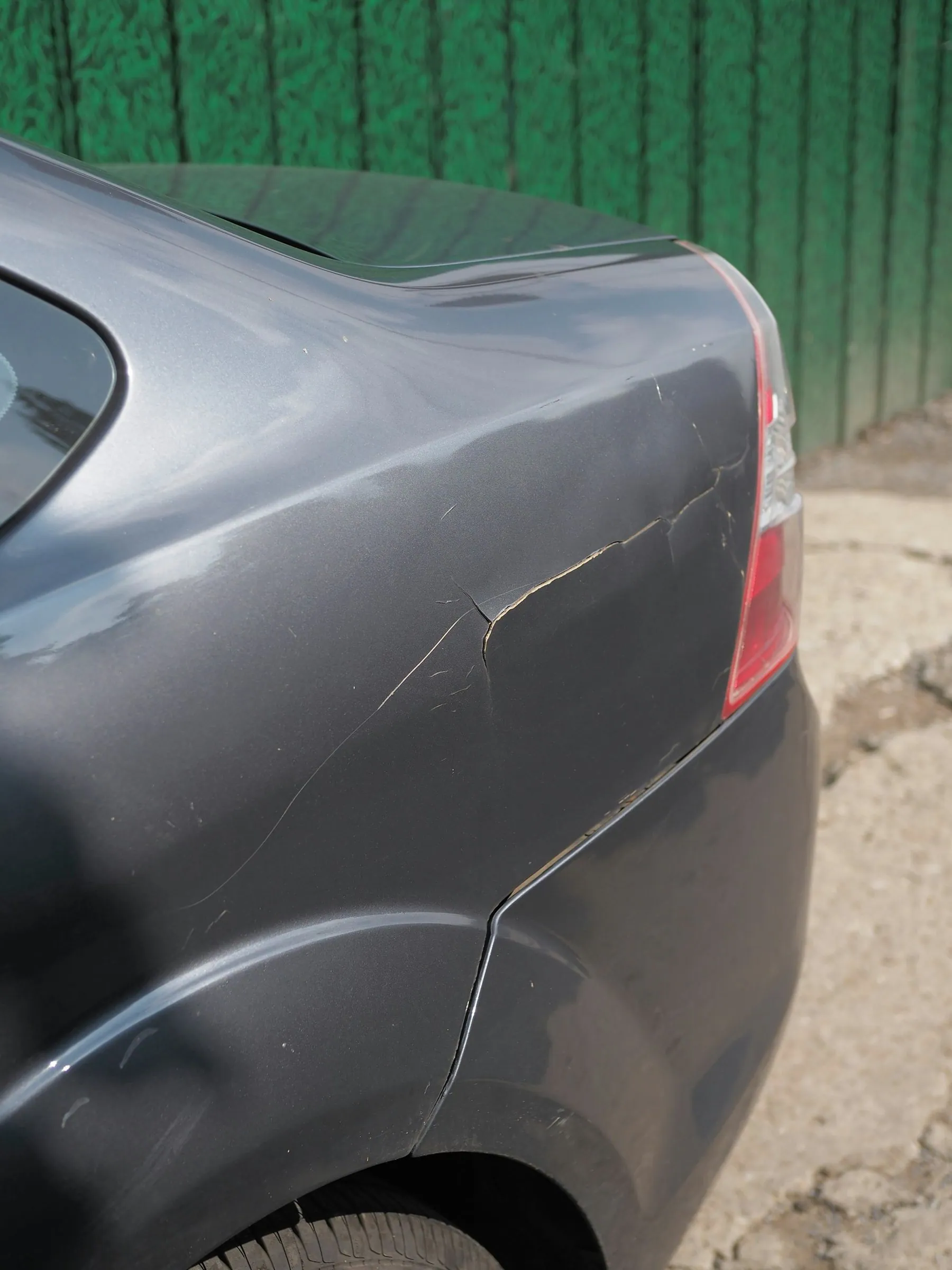 A crease and flaking paint along the rear wing of a grey car, shot close