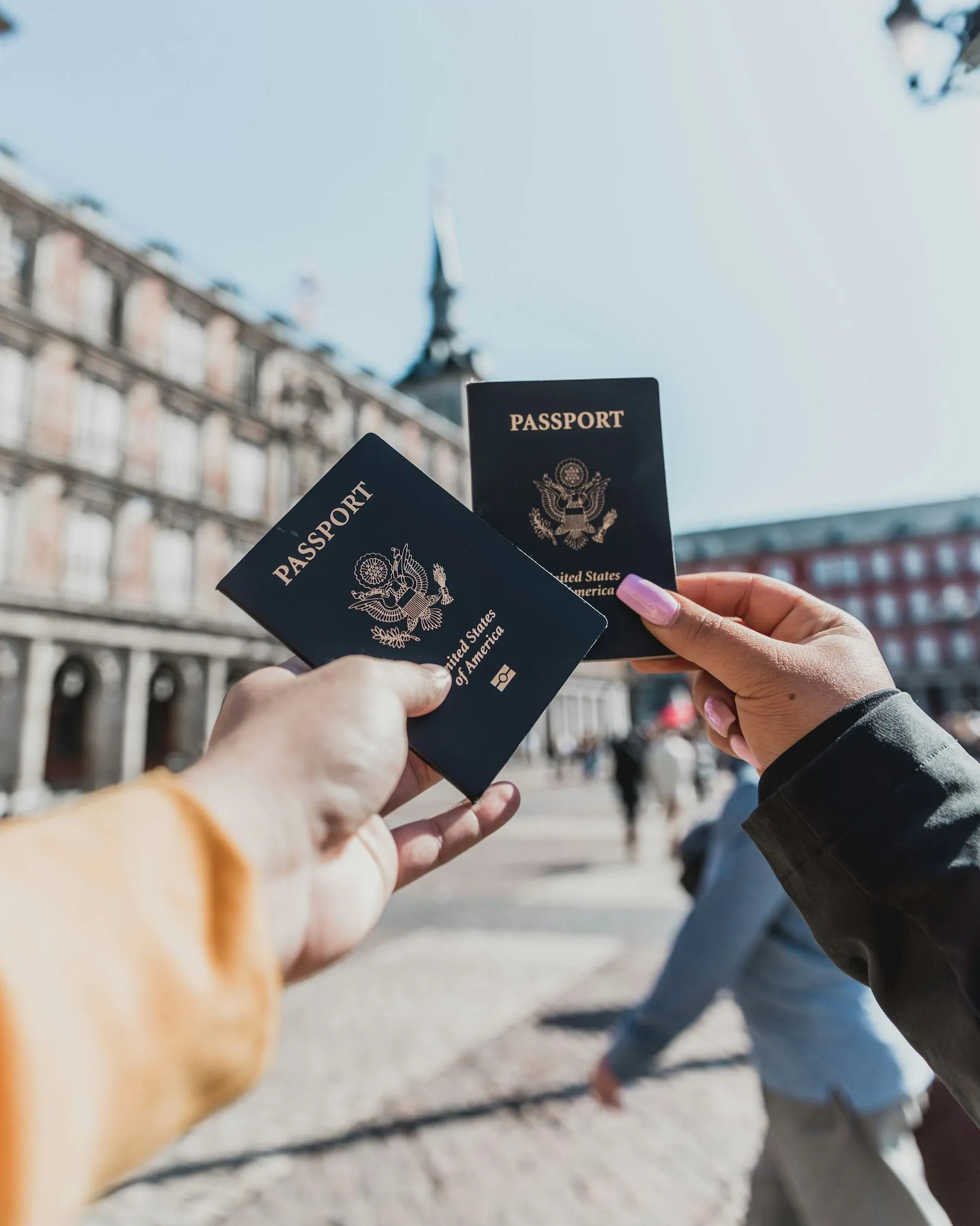 Two hands holding up a pair of passports in front of a city square