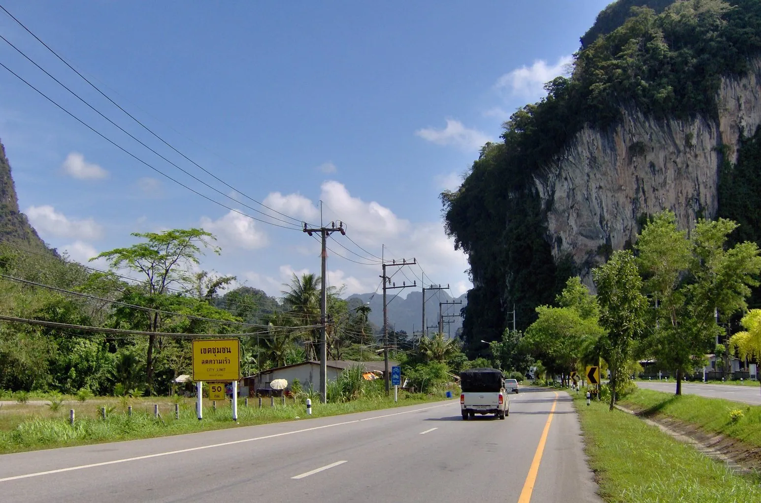 A road near Phang Nga town with jagged limestone karst towers rising directly behind the tree line
