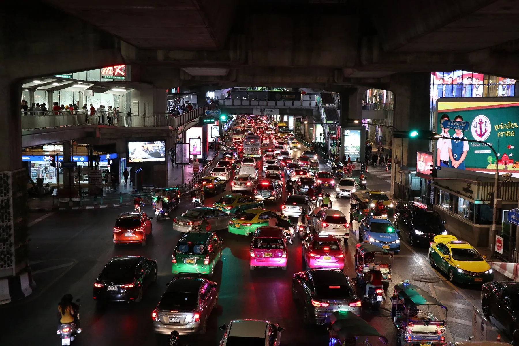 Bumper-to-bumper evening traffic across several lanes in Bangkok, tuk-tuks and taxis wedged among the cars
