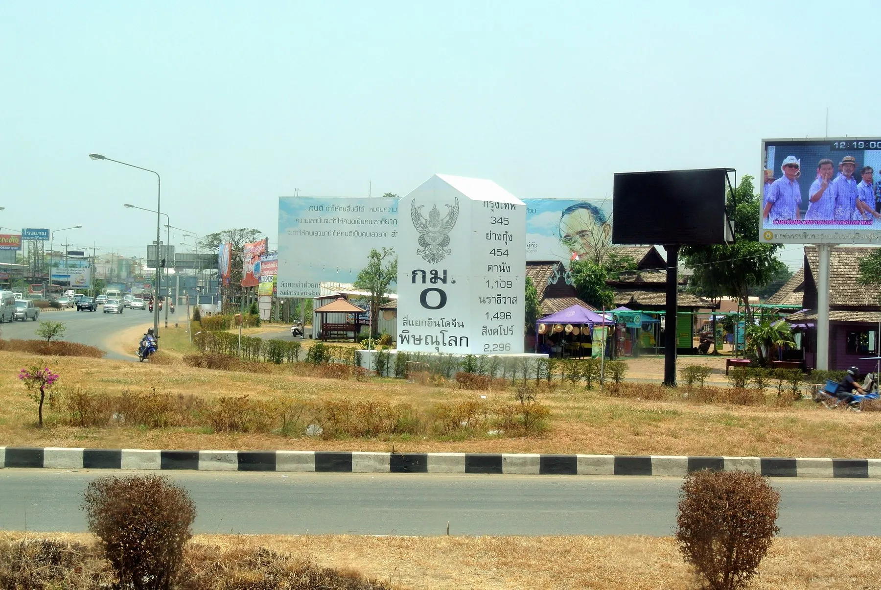 A concrete kilometre milestone on the verge of a highway in northern Thailand with hills beyond
