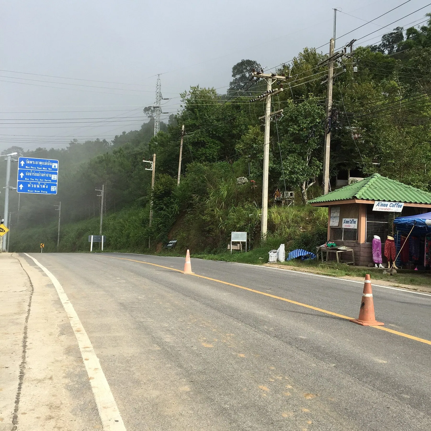 A road through Mae Na Toeng in Pai district with a blue direction sign and wooded hills behind