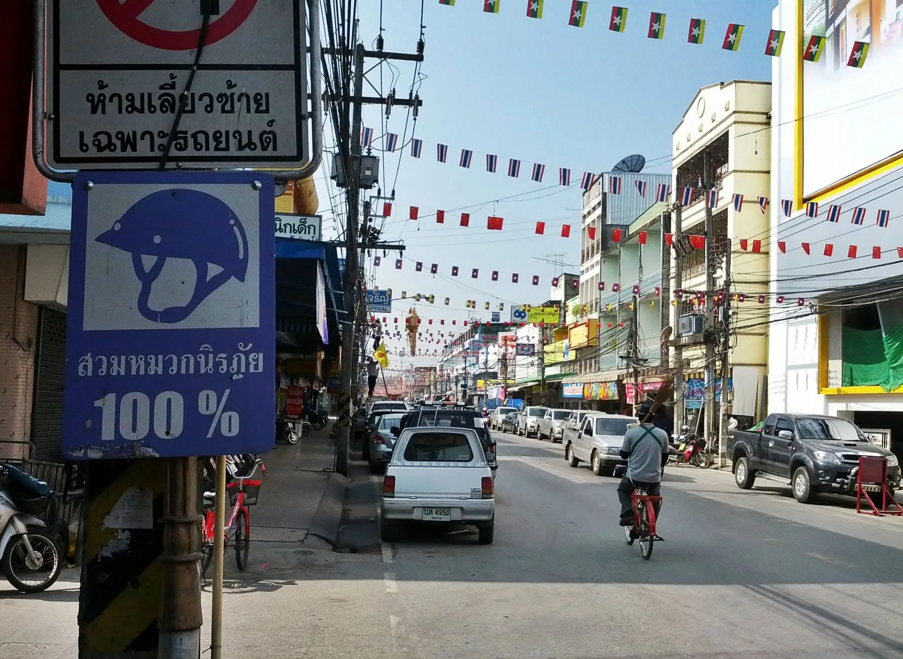 A Chiang Rai street hung with bunting, motorbikes and cars moving between low shopfronts