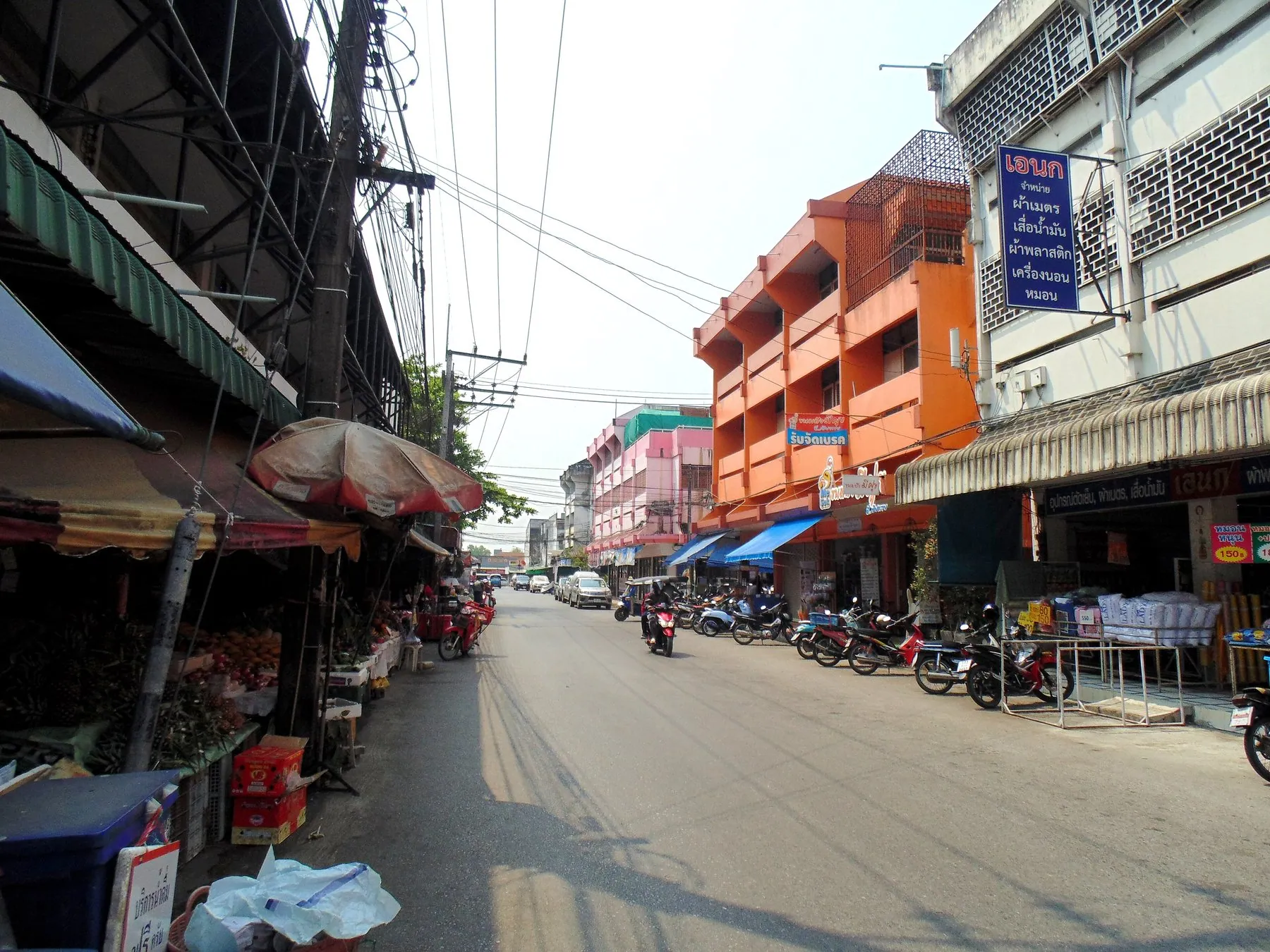A street of orange and cream shophouses in central Chiang Rai with parked cars along the kerb