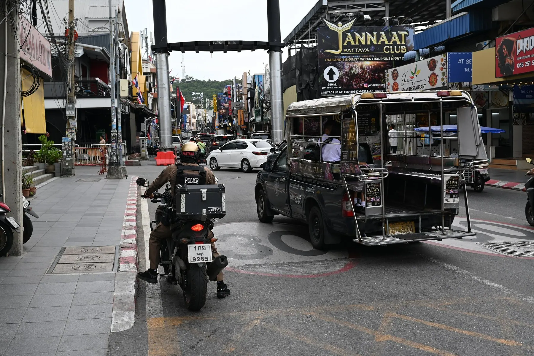 A blue songthaew baht bus stopped on a Pattaya street with a police motorbike waiting behind it
