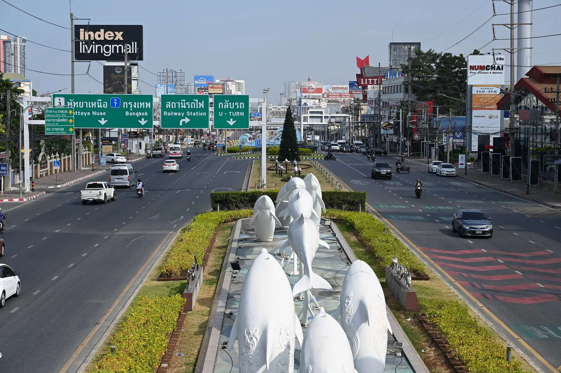 A divided road in Pattaya with cars, pickups and motorbikes passing white horse statues on the central reservation