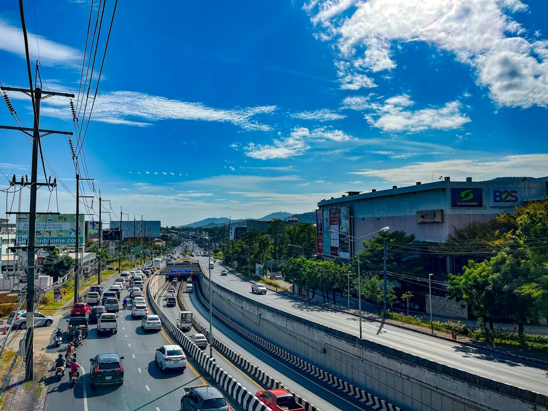 Traffic queuing at an underpass on a wide road in Phuket town under a bright blue sky