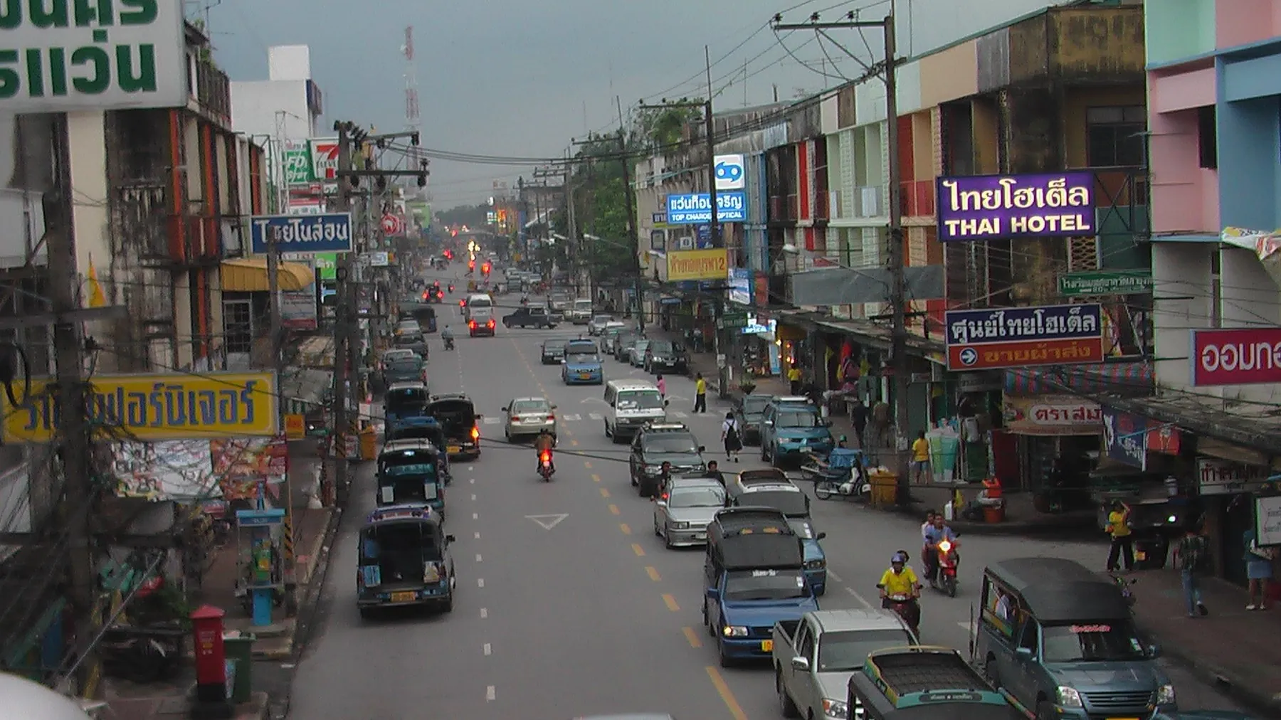 A busy street in downtown Nakhon Si Thammarat with cars, motorbikes and pickups between shophouses