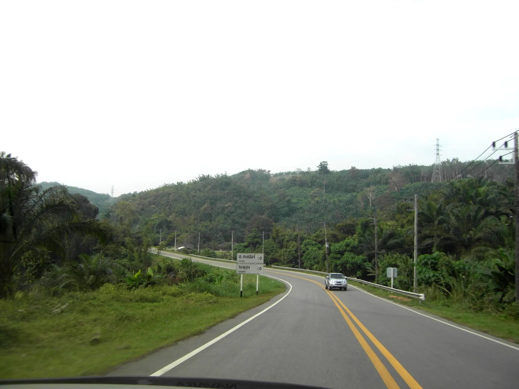 A road dropping away downhill through dense green forest in southern Thailand
