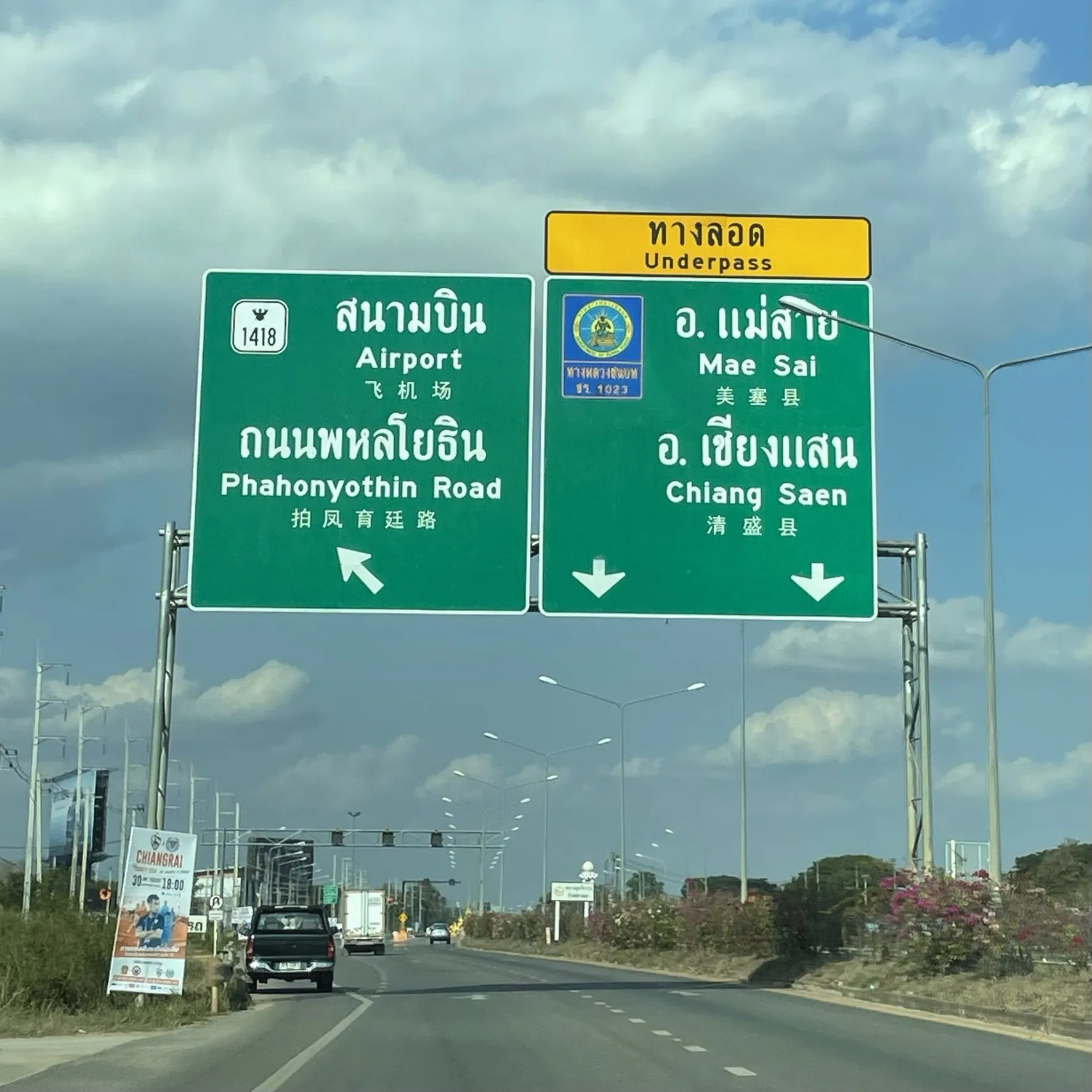 A green overhead direction sign in Thai, English and Chinese pointing towards Chiang Saen on a road out of Chiang Rai