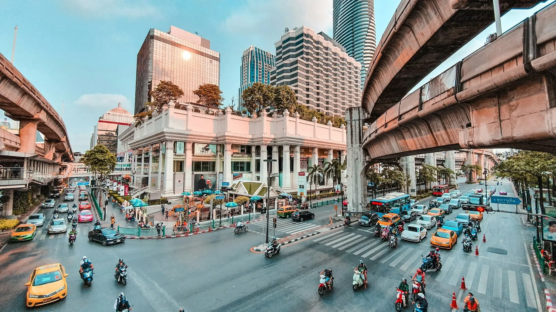 Cars and taxis parked along the kerb of a Bangkok street under an elevated expressway