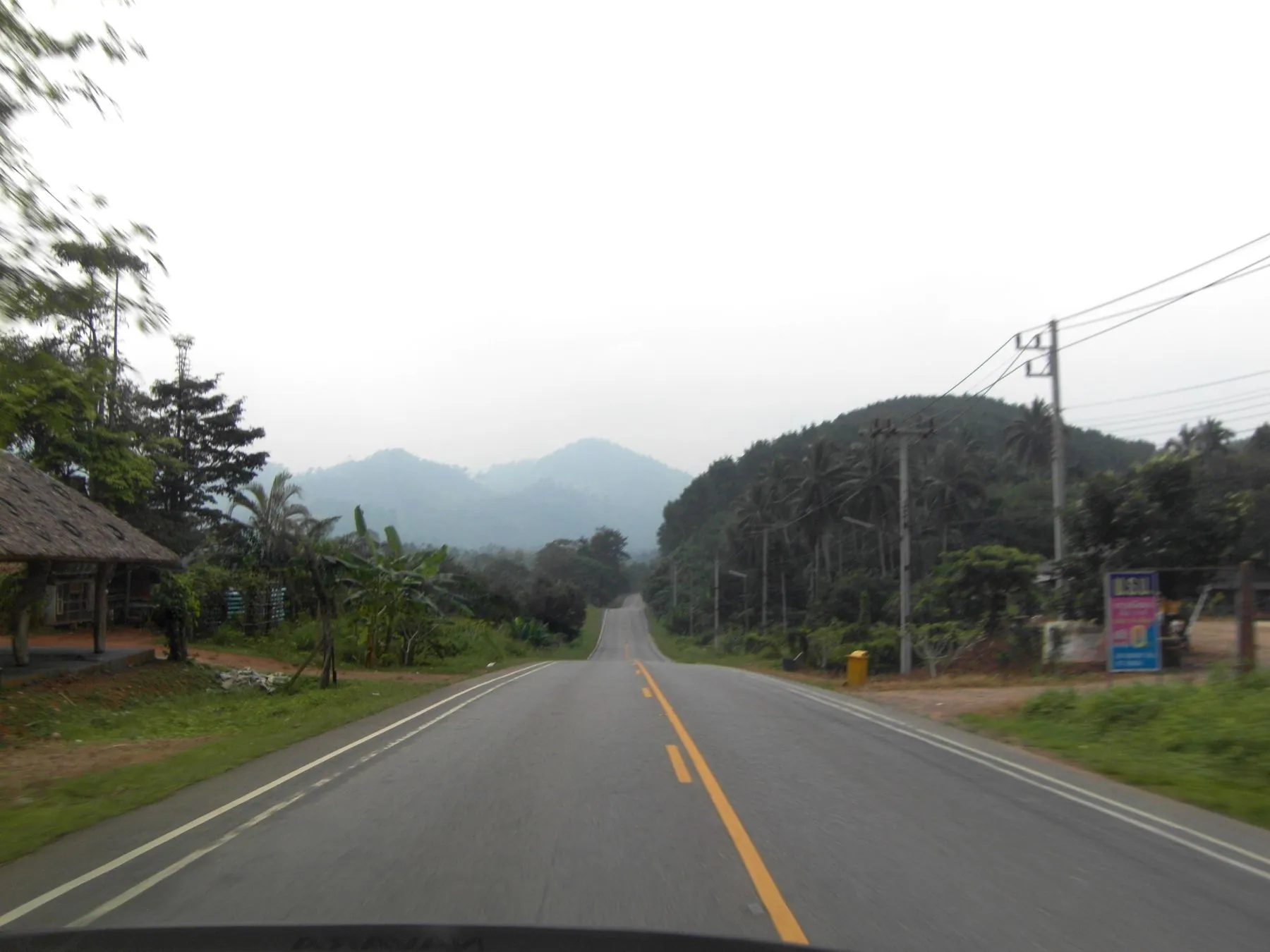 A straight stretch of highway in Chumphon province with forested hills rising ahead