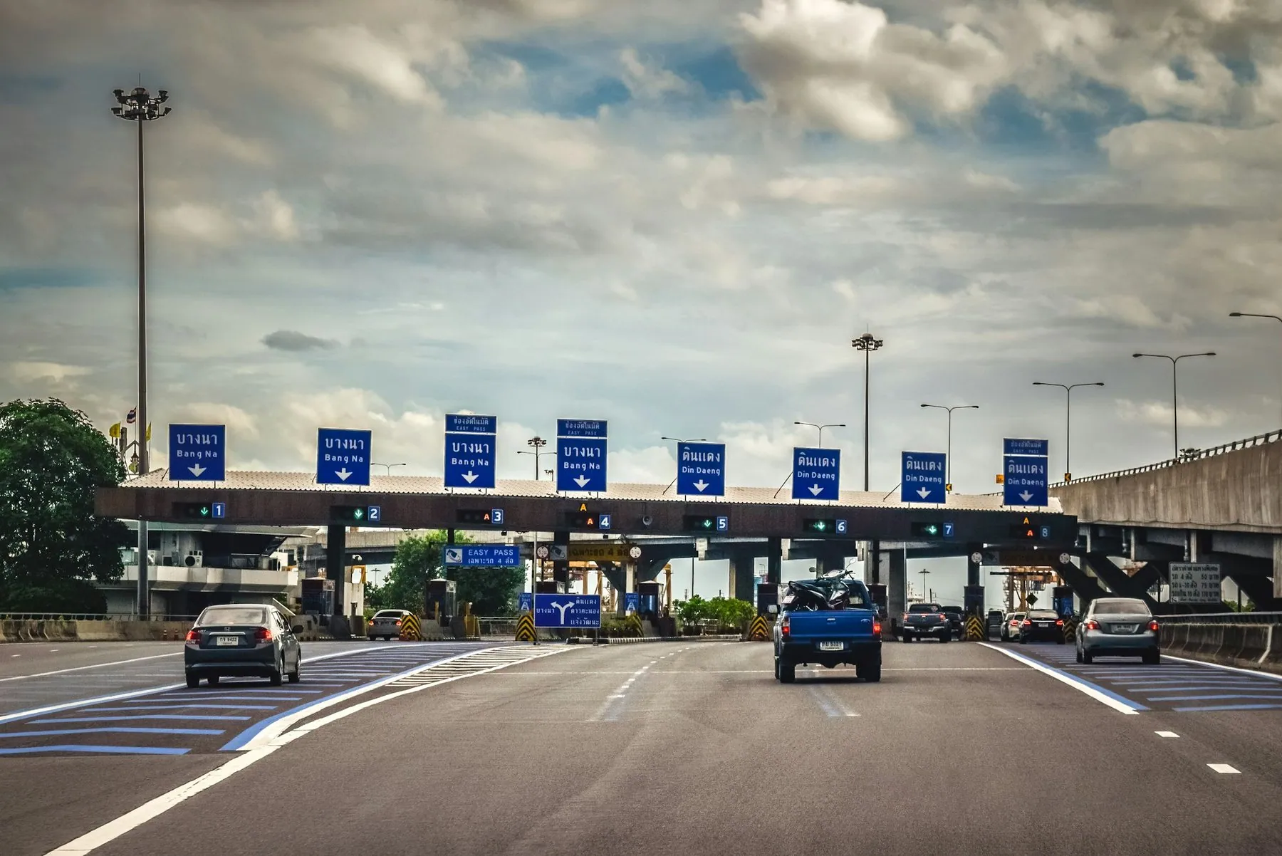 A row of toll booths across a Bangkok expressway, blue lane signs in Thai above each gate