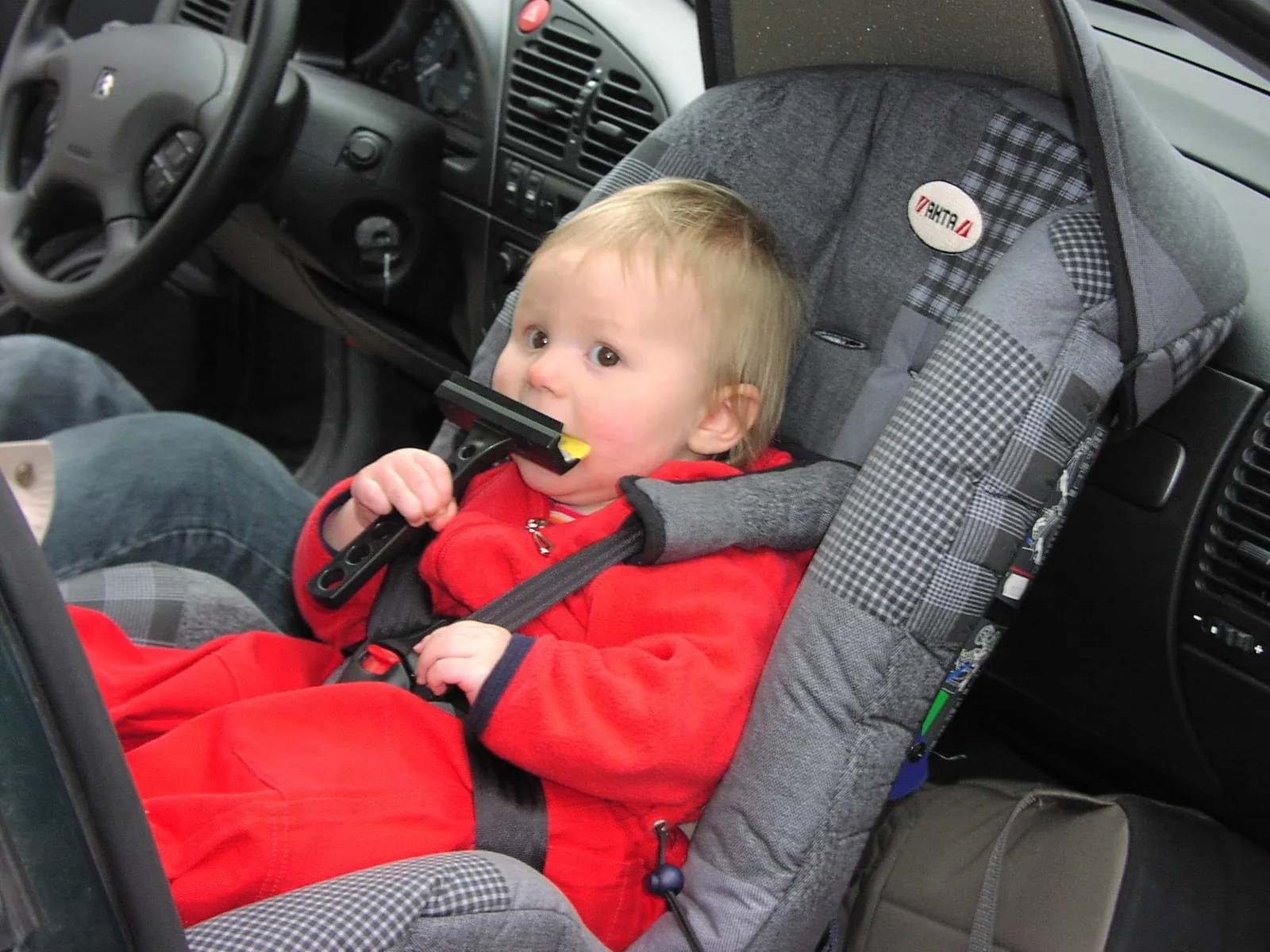 A rear-facing infant carrier fitted on a car seat with its harness laid open