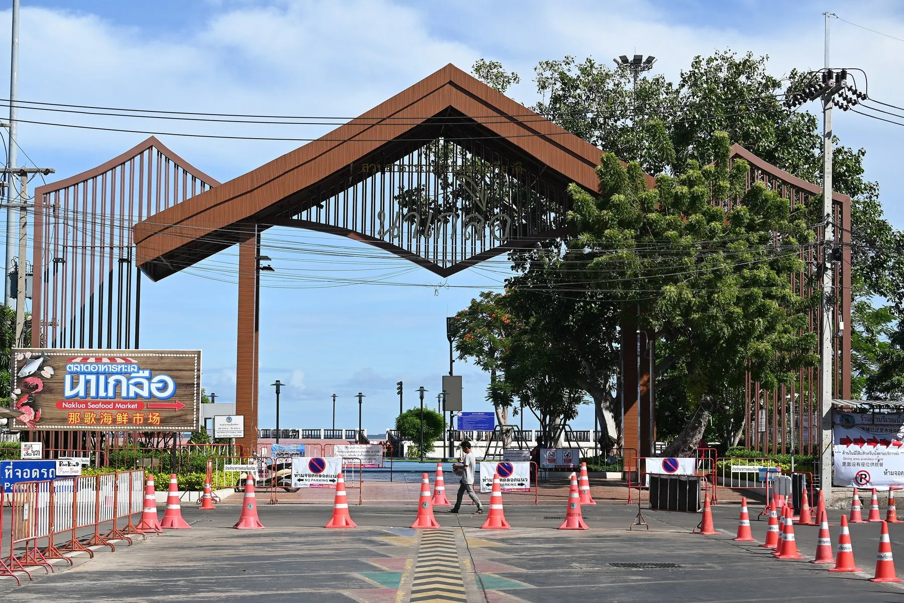 Cones and barriers funnelling cars through a single lane beneath a wooden archway in Thailand
