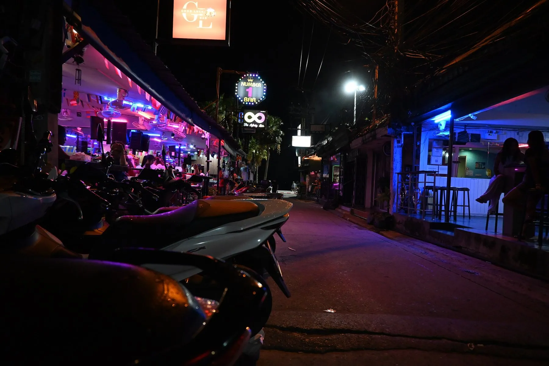 Scooters parked along a Thai bar street glowing purple and blue after dark