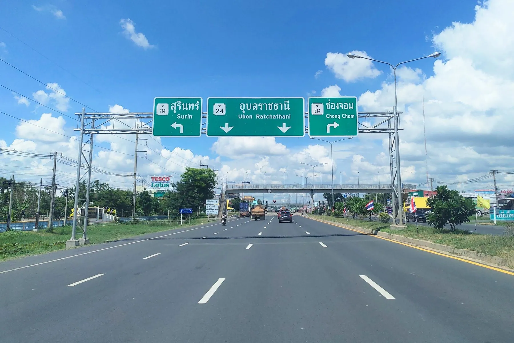Traffic on Thai national highway 24 running beneath a green overhead direction gantry at Prasat, Surin