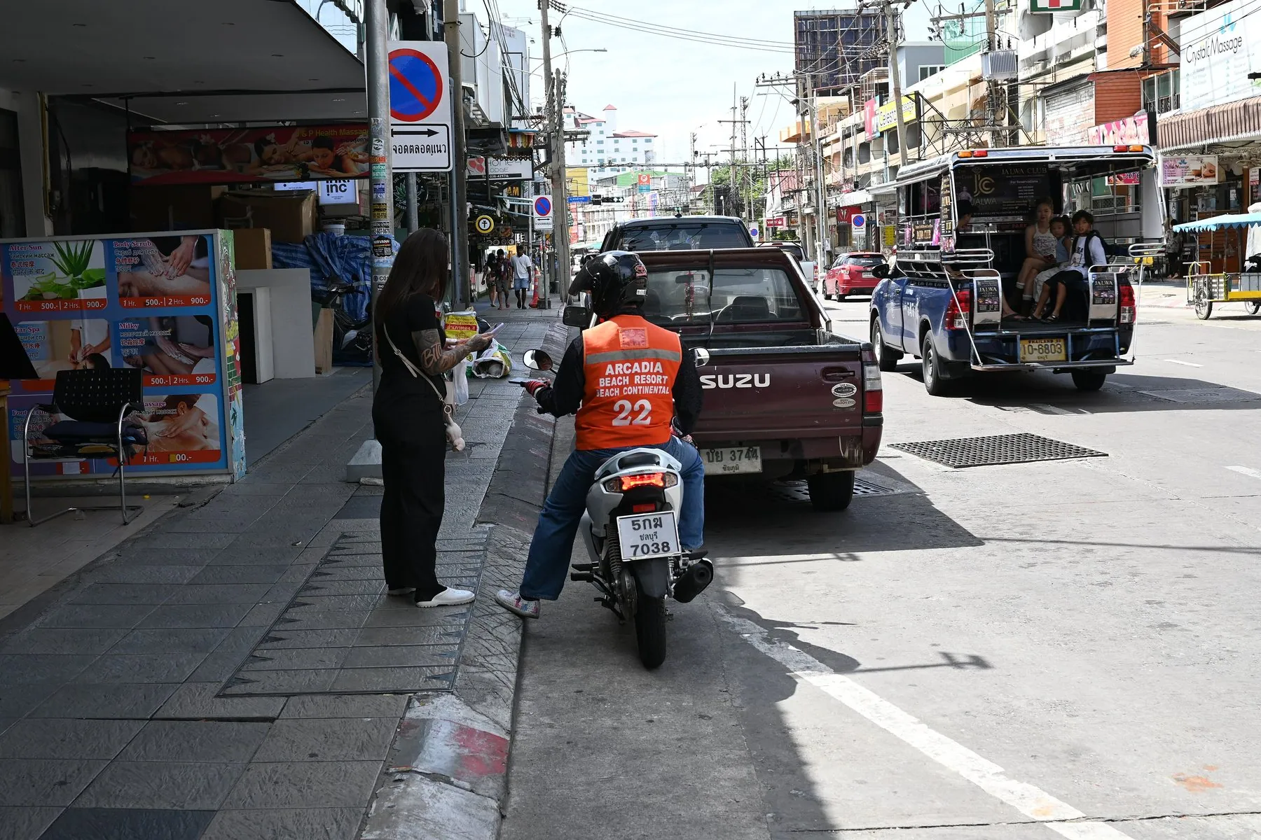 A motorcyclist in an orange vest waiting behind a pickup truck on a busy Thai street