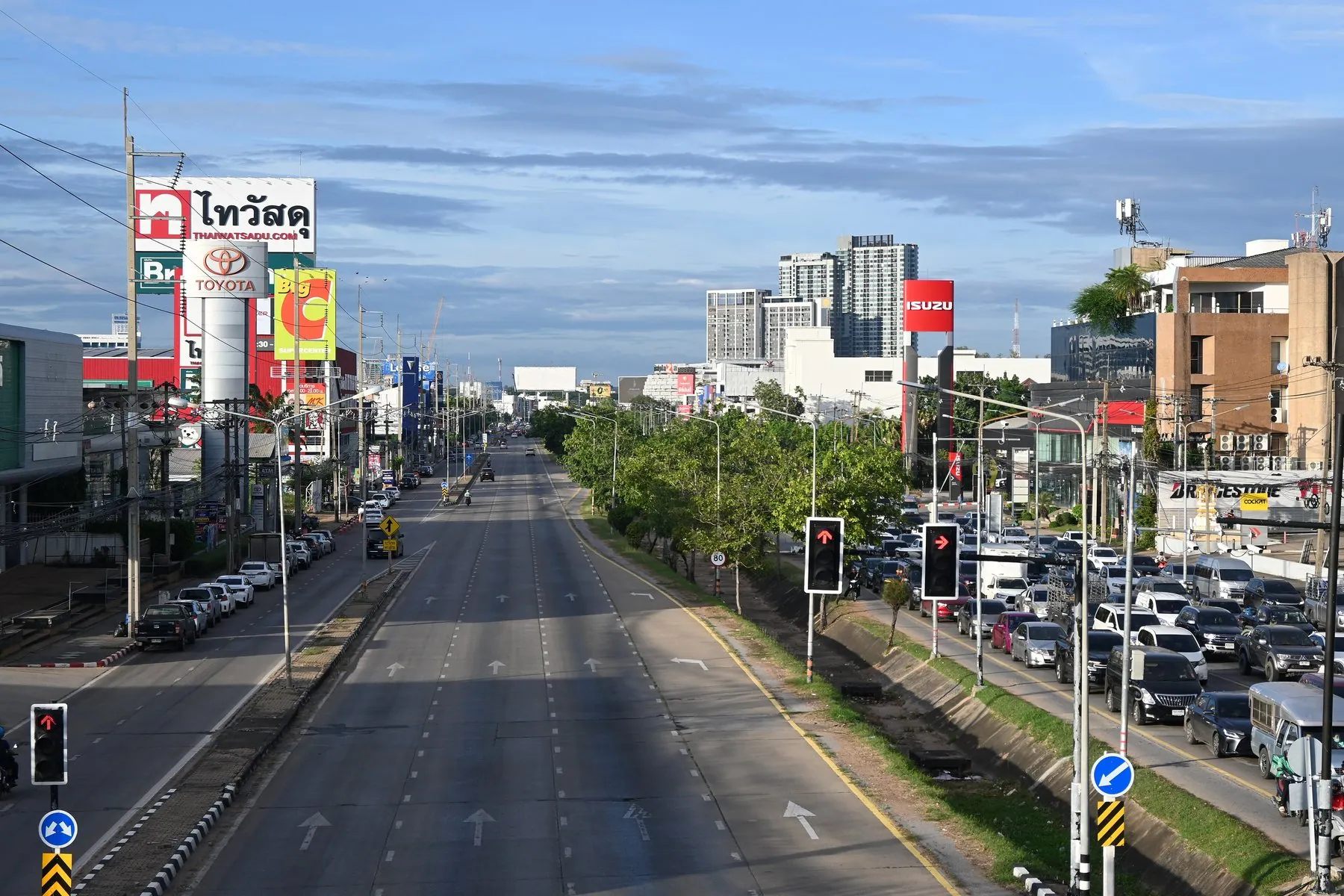 A wide Thai avenue with empty lanes on one carriageway and nose-to-tail traffic on the other