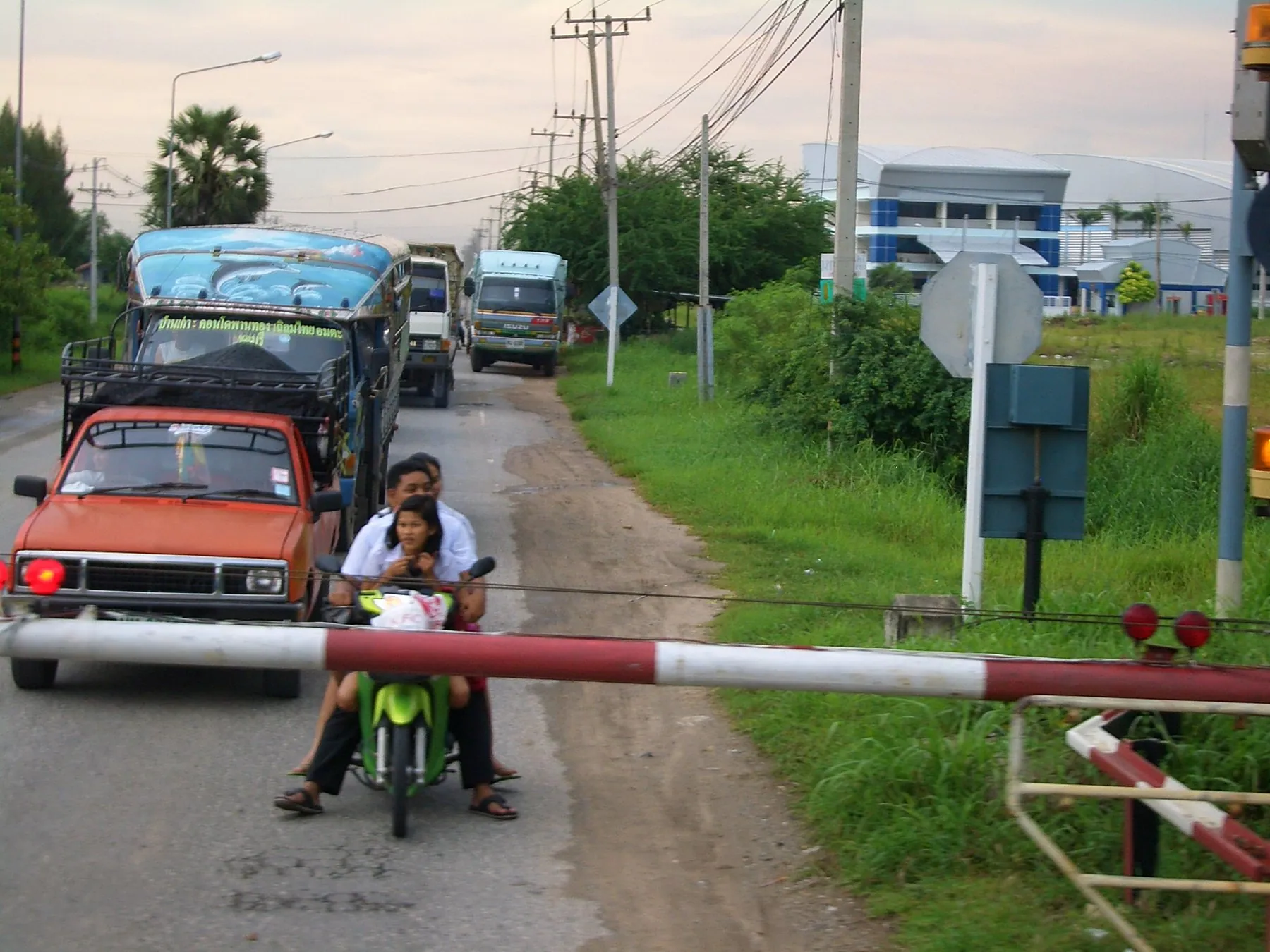 Cars and motorbikes held at a railway crossing near Si Racha as the barrier comes down