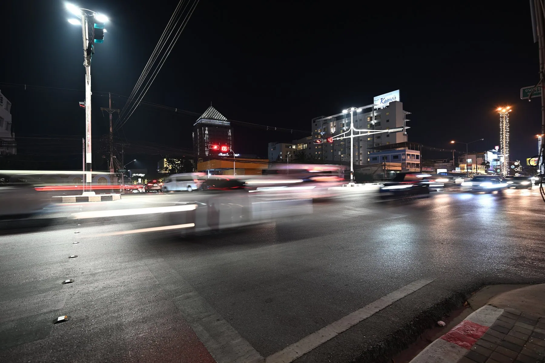 Headlight and indicator trails blurring across a busy Thai city junction at night