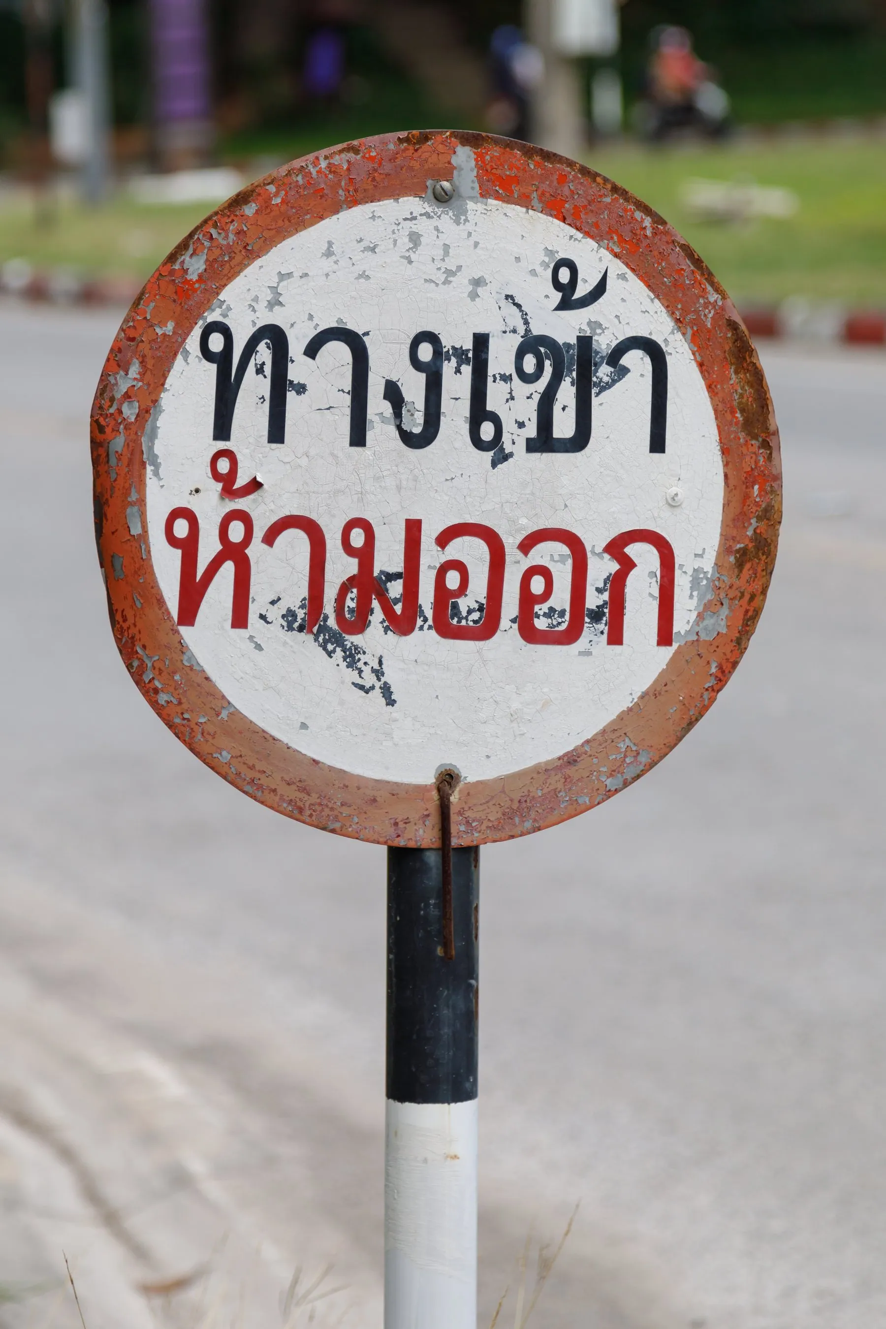 A red-and-white prohibitory sign on a pole at Chiang Mai University with a Thai-script plate beneath it