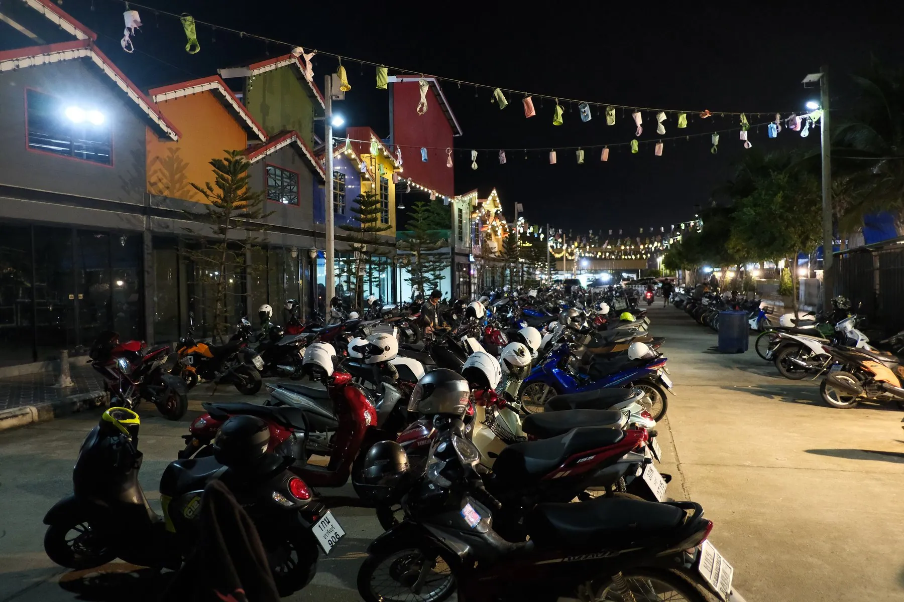 Rows of motorbikes parked nose-in along a brightly lit Thai street at night
