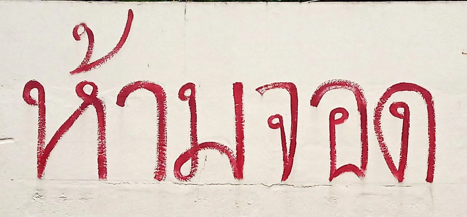 A hand-painted Thai no-parking sign fixed to a wall above a strip of roadside kerb