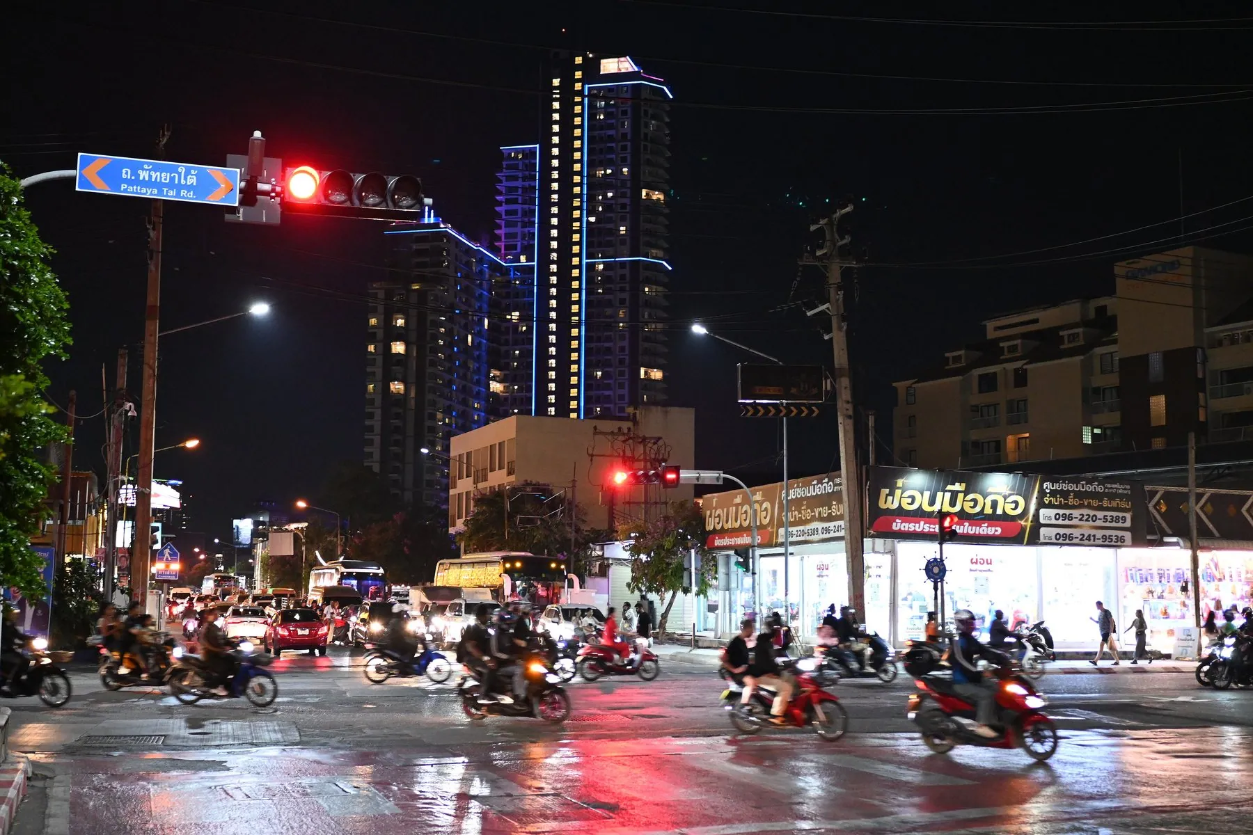 Scooters weaving through a neon-lit street in Ban Phatthaya Tai after dark