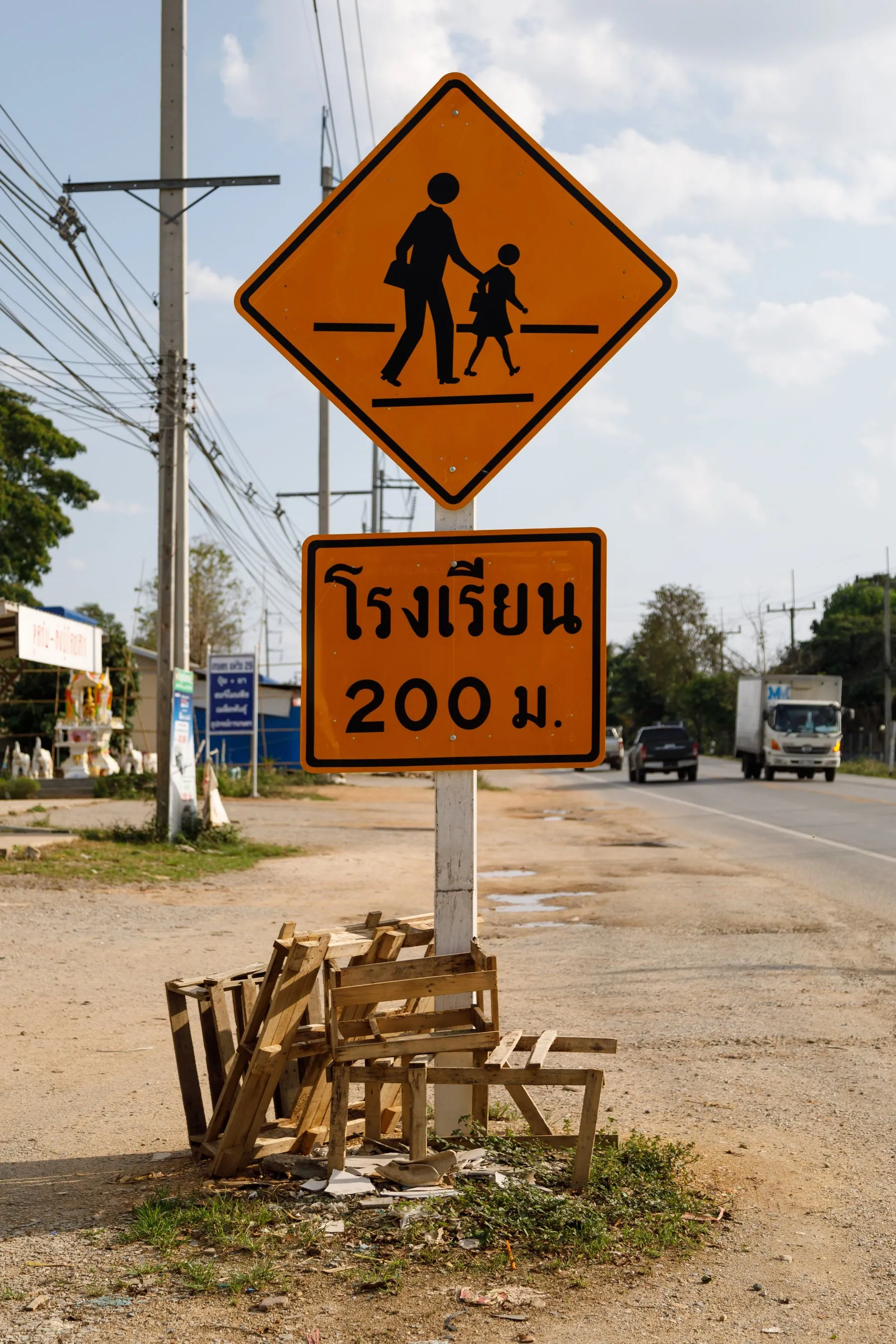 A yellow diamond children-crossing warning sign on a Thai roadside pole