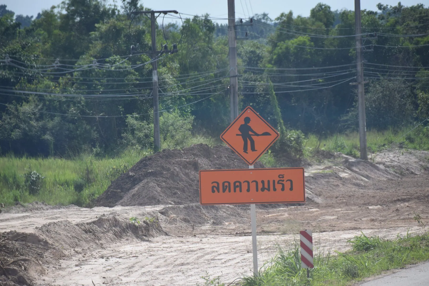 An orange Thai roadworks warning board propped on the carriageway ahead of an unmarked hazard