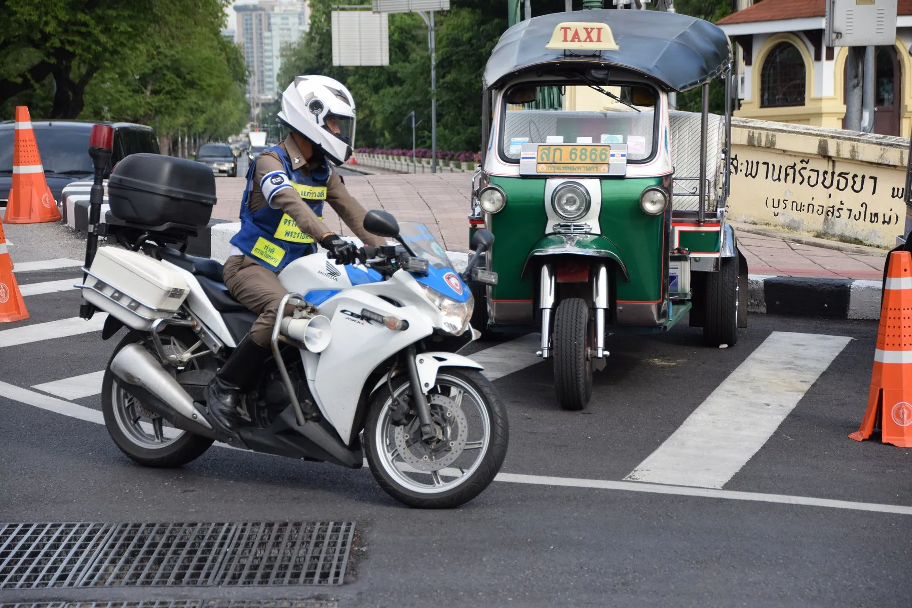A Thai police motorbike parked on a street with its blue lights on the rack behind the seat