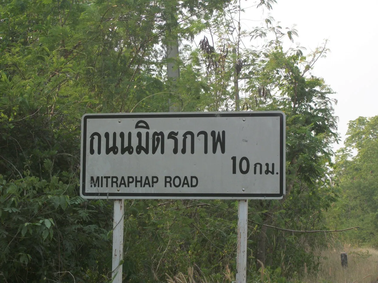 A small blue kilometre marker beside an empty rural Thai road