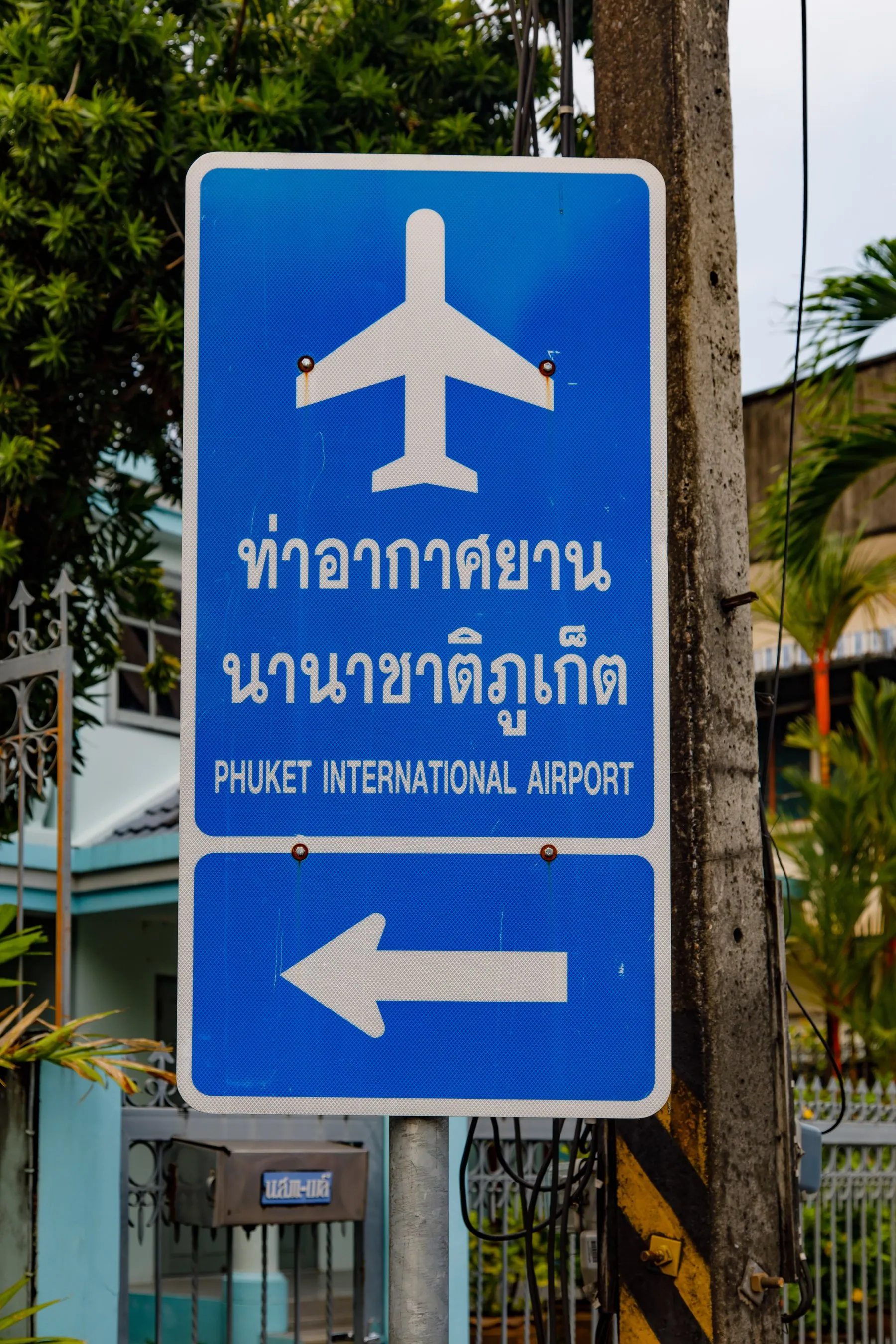 A blue Thai directional sign with a white arrow mounted high on a roadside post