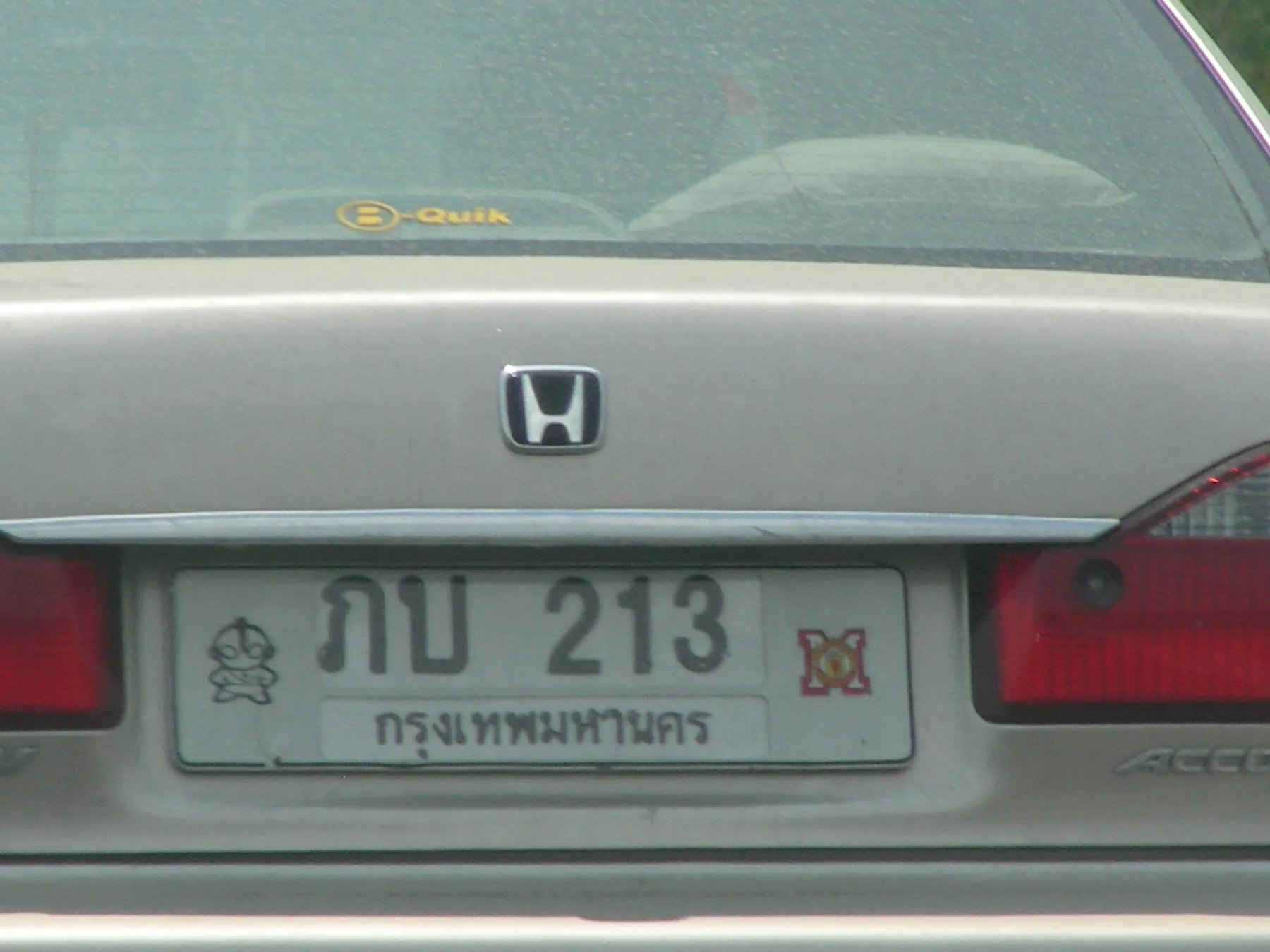 A white Thai number plate with black Thai characters and the current tax sticker beside it