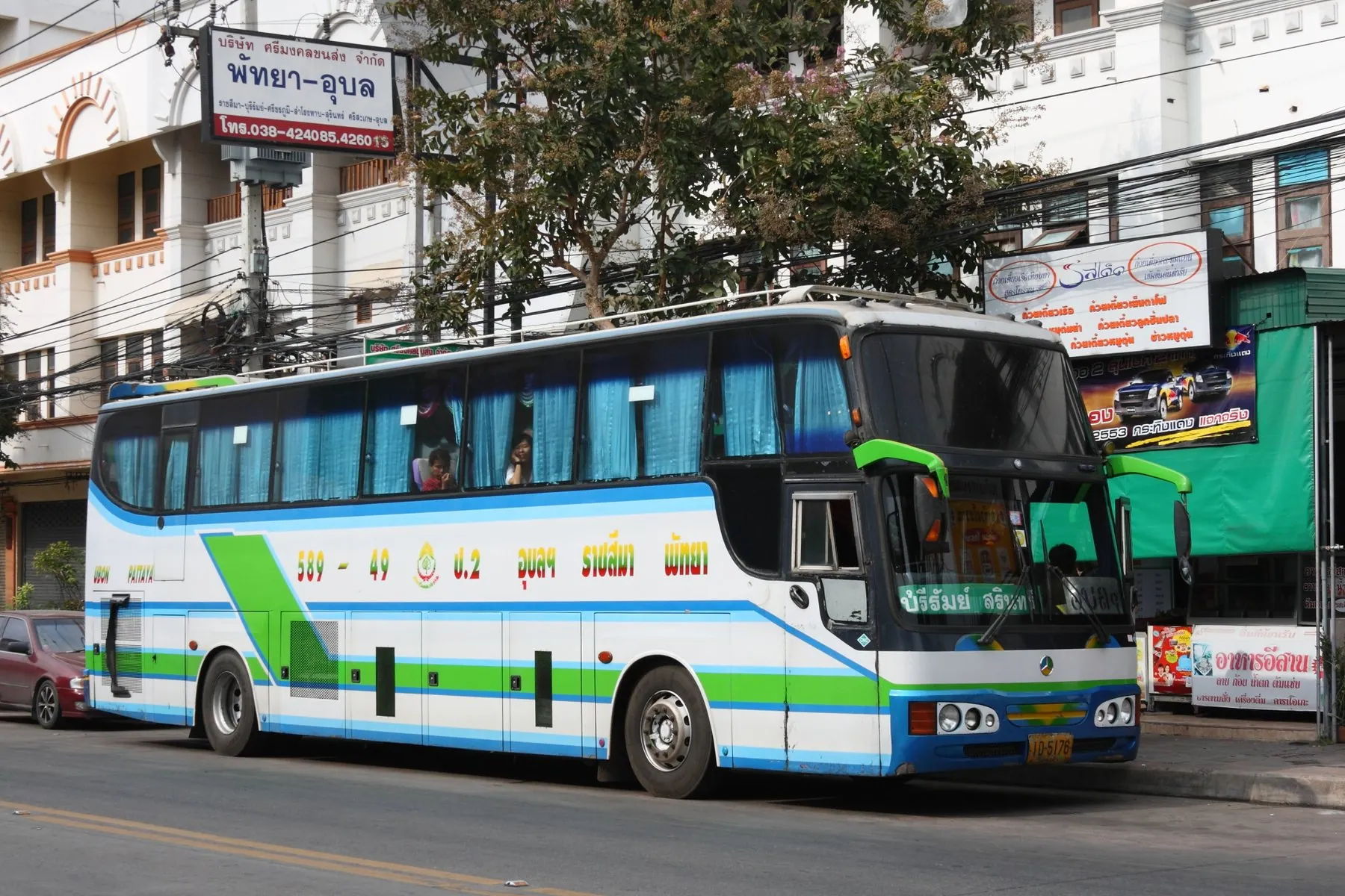 A green and white intercity coach standing in a Thai street beneath shop signs in Thai script