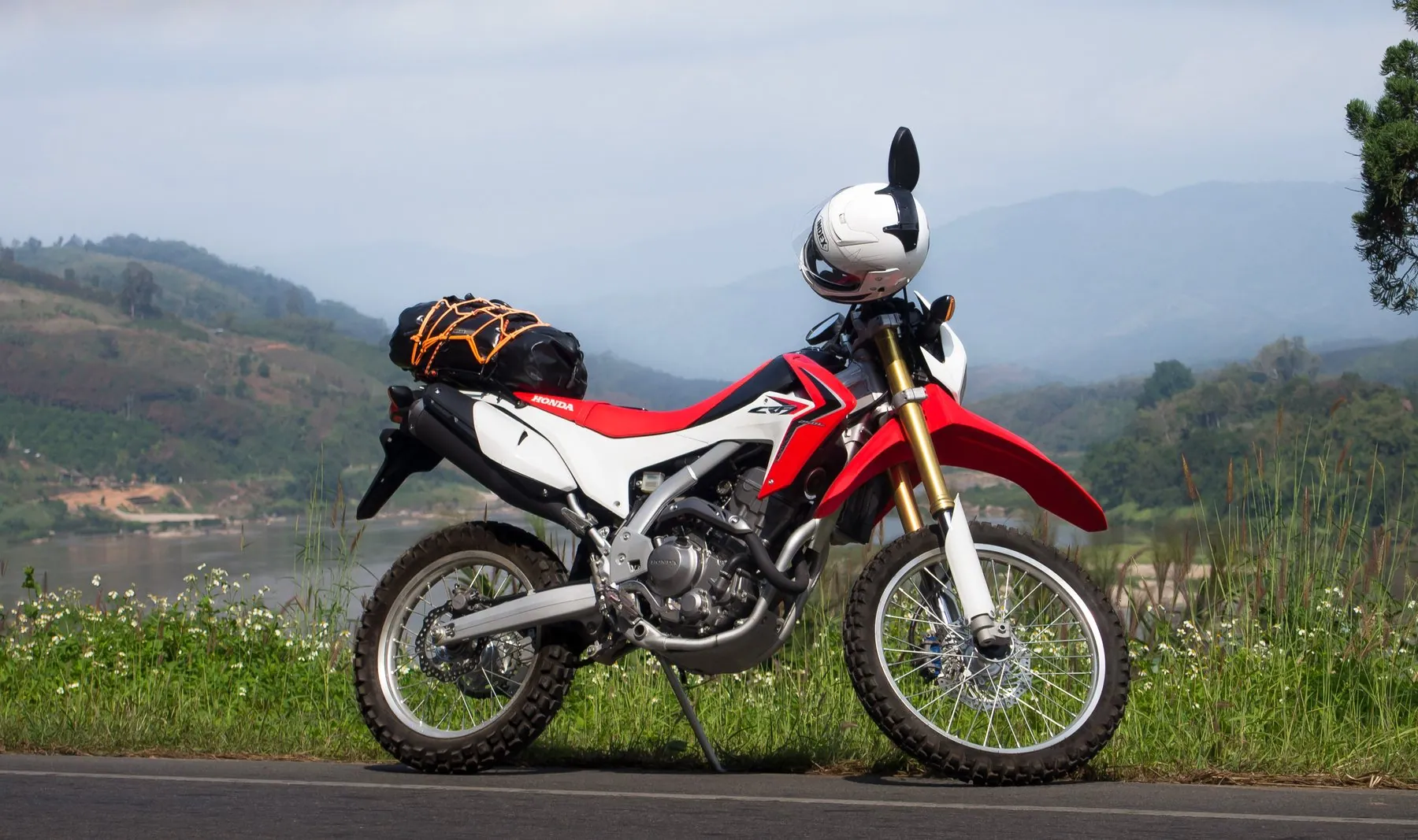 A red and white trail bike with a dry bag and helmet strapped to the rear rack, the Mekong behind it