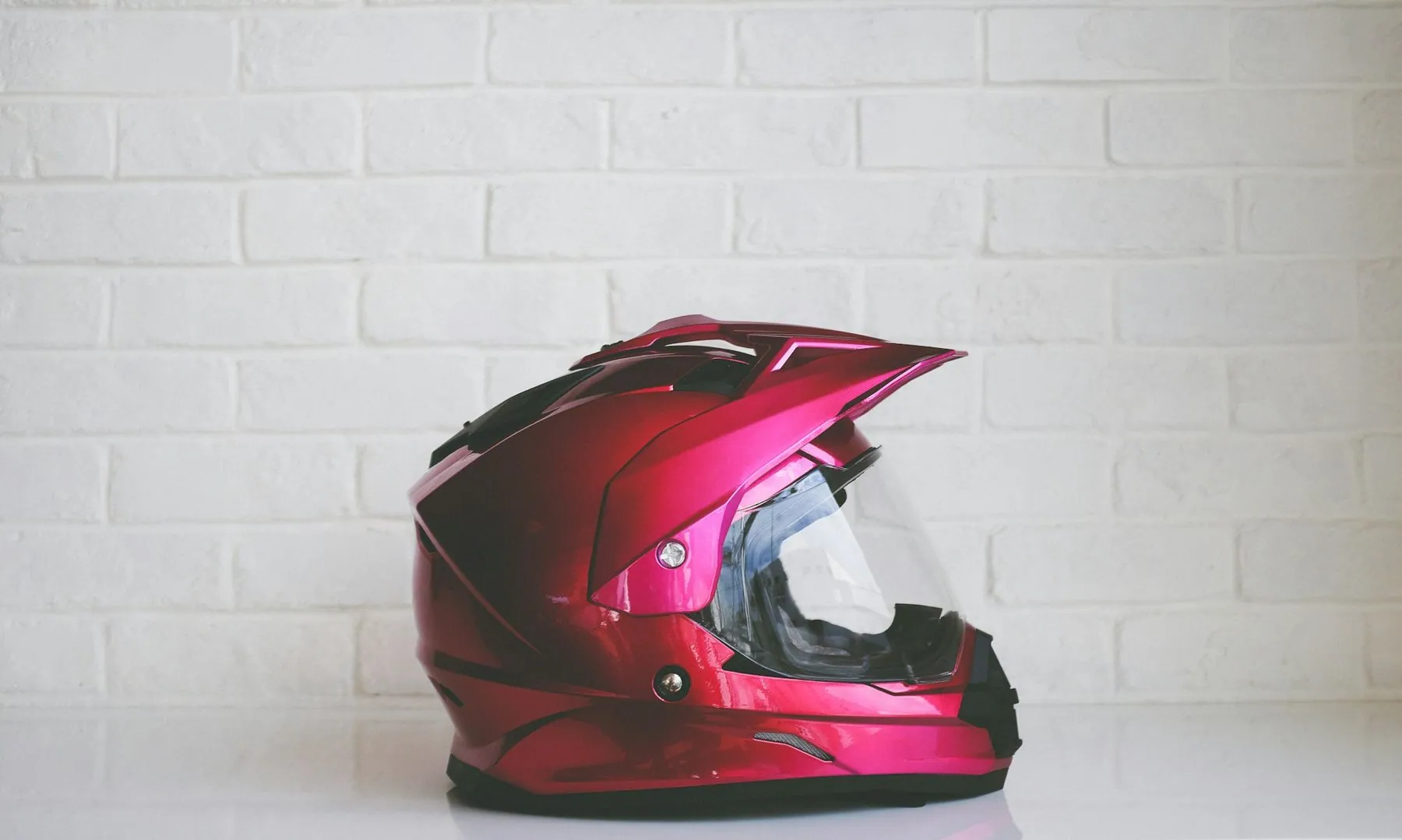 A red full-face helmet with the visor closed, standing on a plain surface against a white brick wall