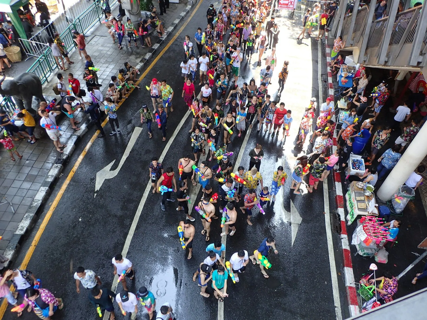 A dense Songkran crowd packed across a closed Bangkok street, water guns raised and the road soaked