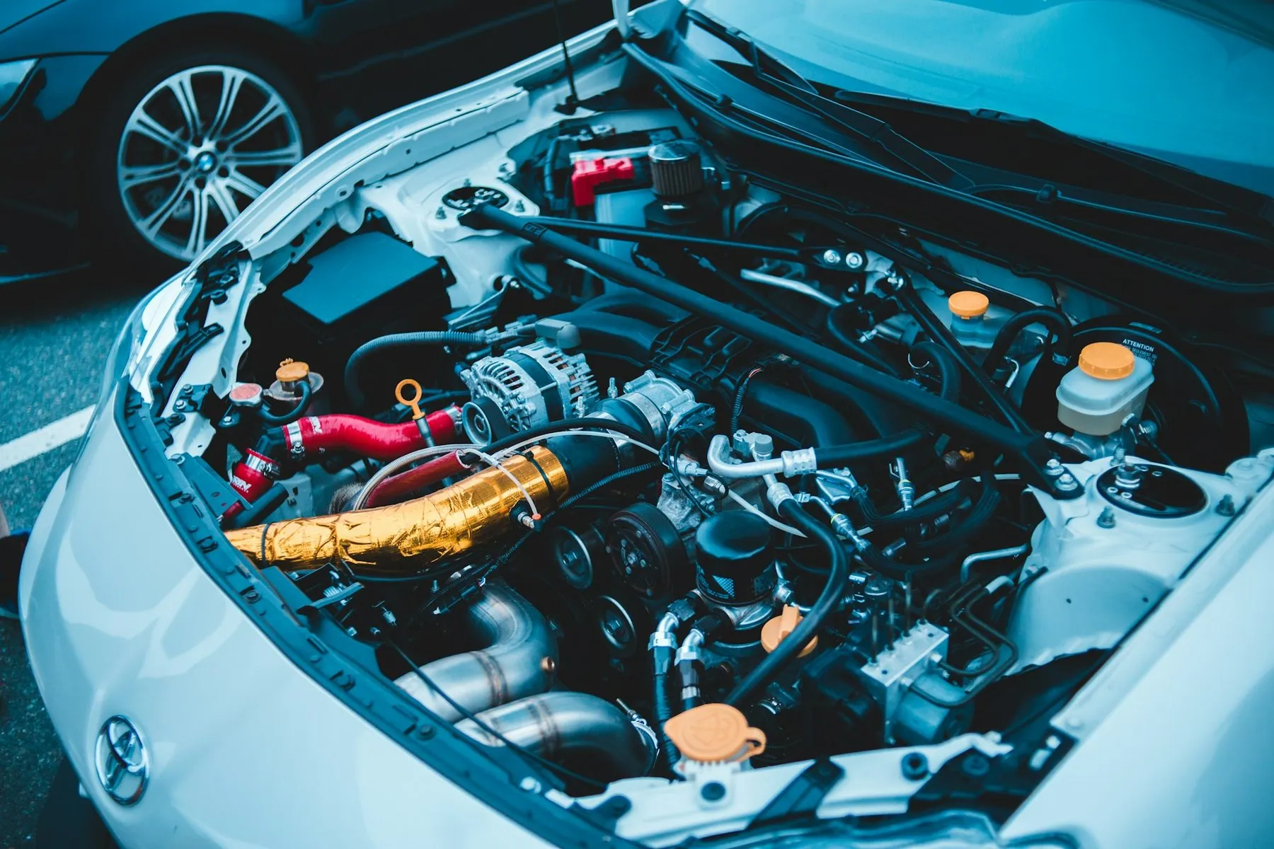 The engine bay of a pale blue car with the bonnet raised, coolant and washer reservoirs in the foreground