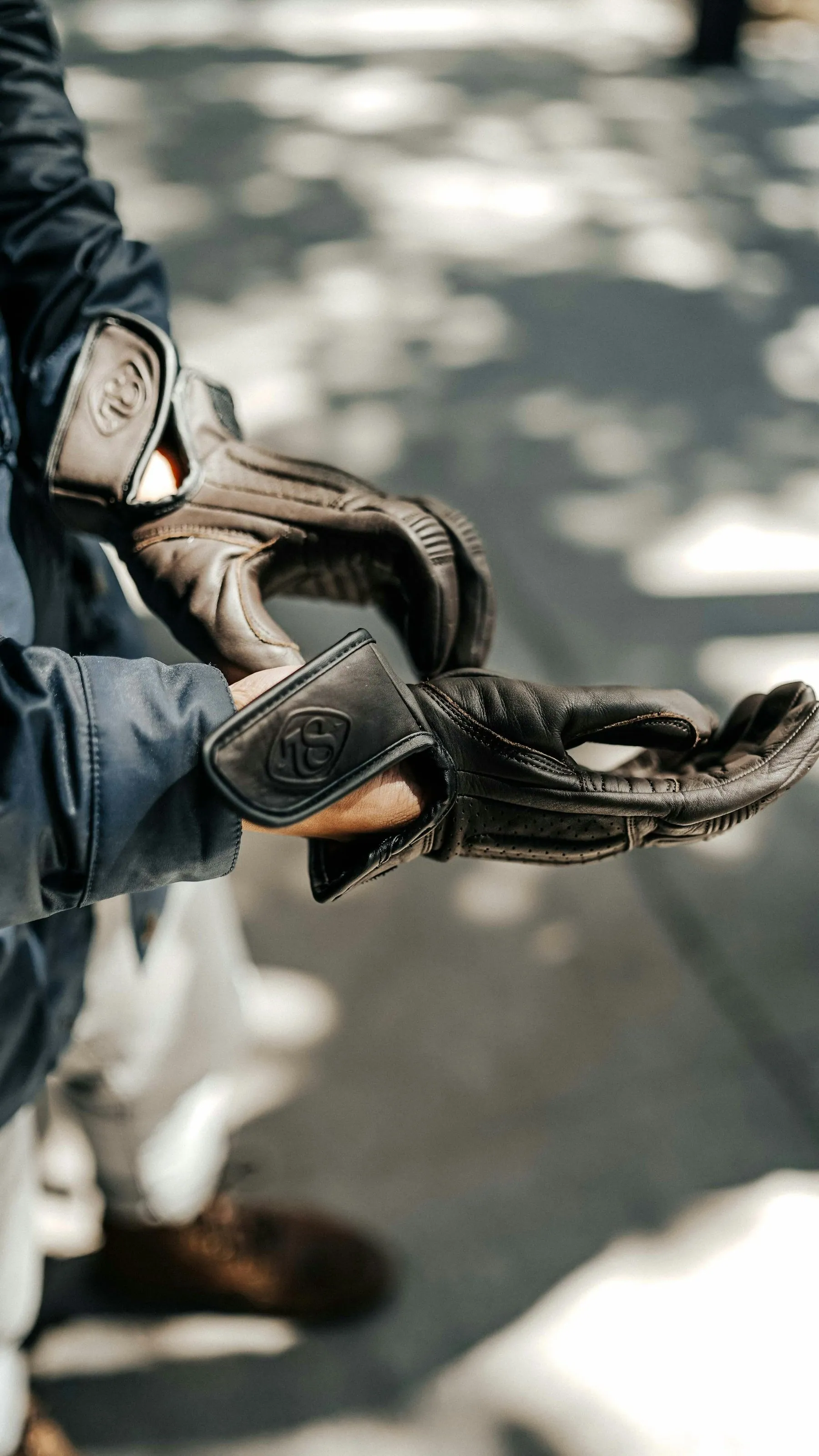 A rider pulling on a leather glove, ankle boots and the kerb visible below