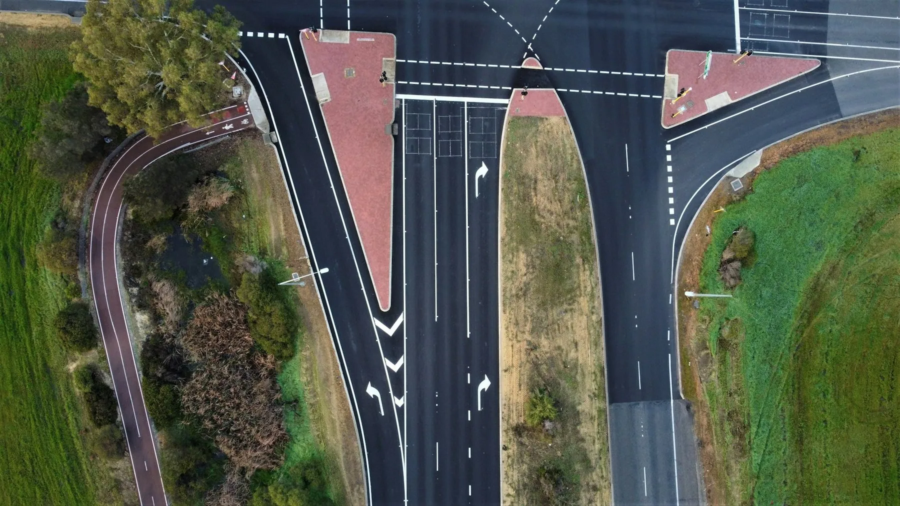 A road intersection seen from directly overhead, lane arrows and stop lines painted on the tarmac