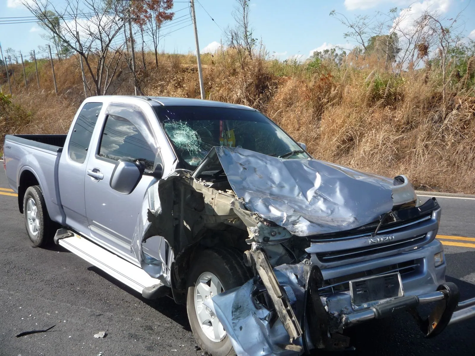 A silver pickup with its whole front nearside crushed, standing on the verge of a rural road in Phetchabun