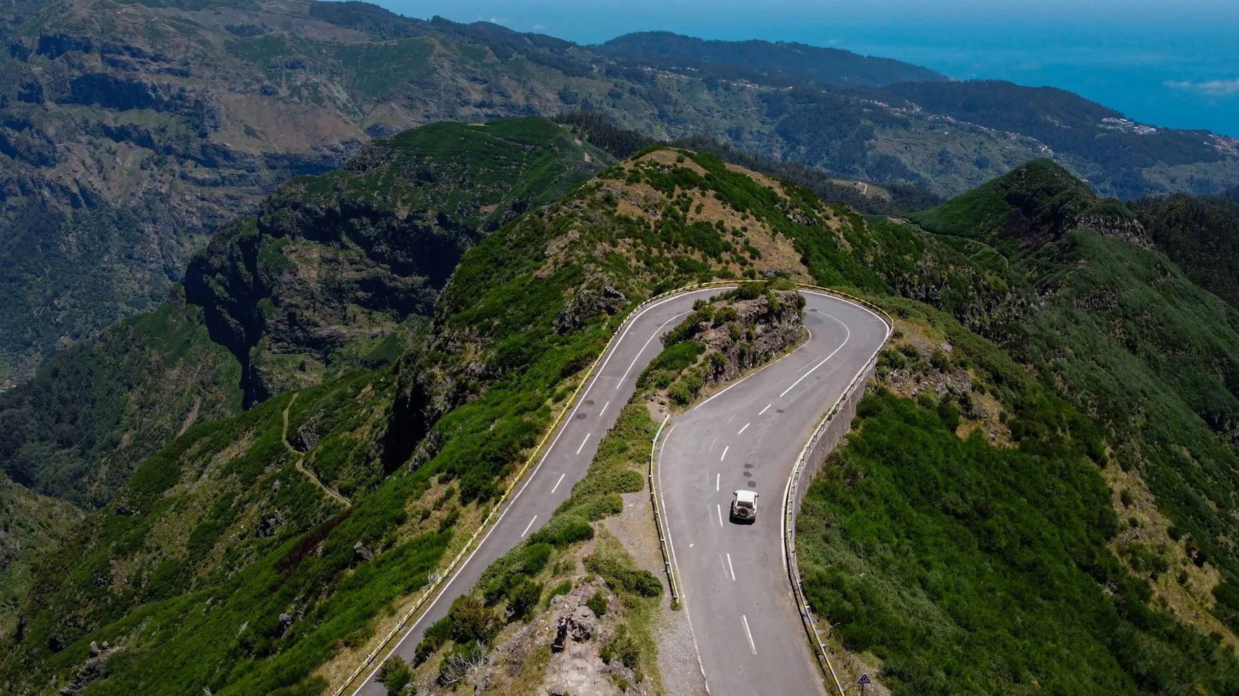 A single car working its way along a road that switchbacks down a green mountainside